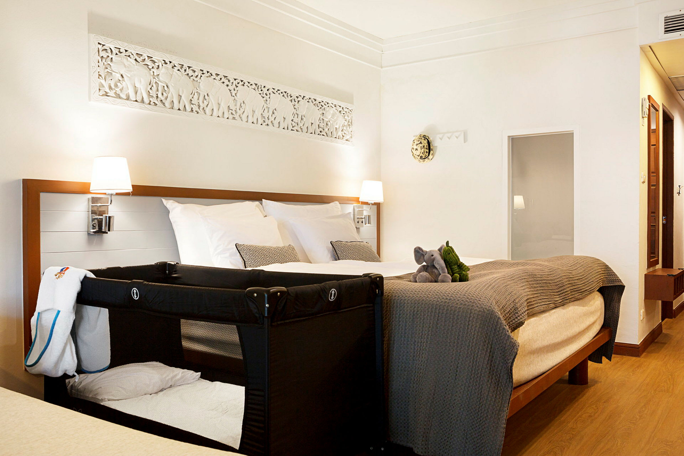 Hotellrum med en dubbelsäng, en barnsäng och två mjukisdjur på sängen. (AI-genererad text)