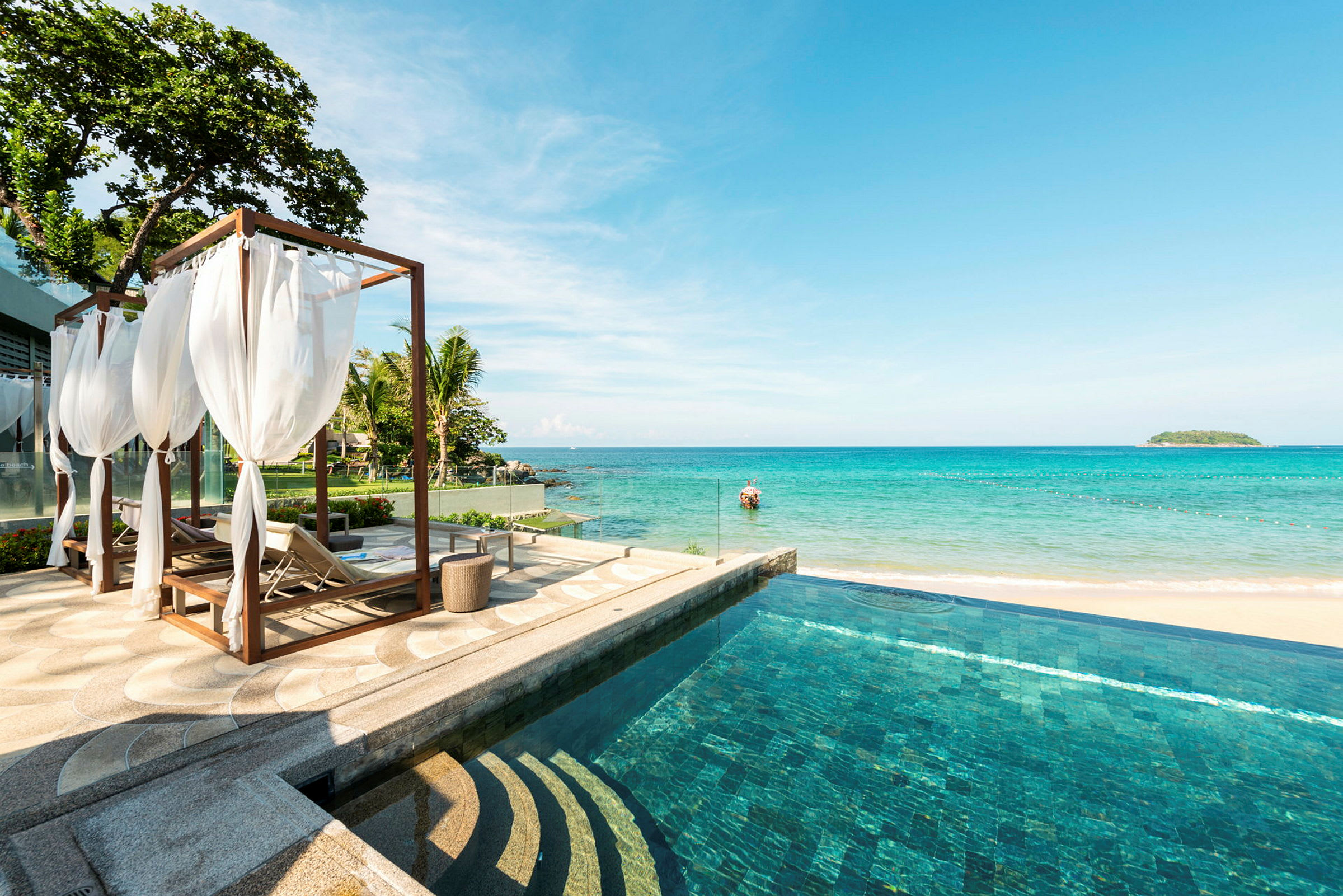 Utsikt över en pool med havet i bakgrunden, samt solstolar och en cabana med vita gardiner. (AI-genererad text)