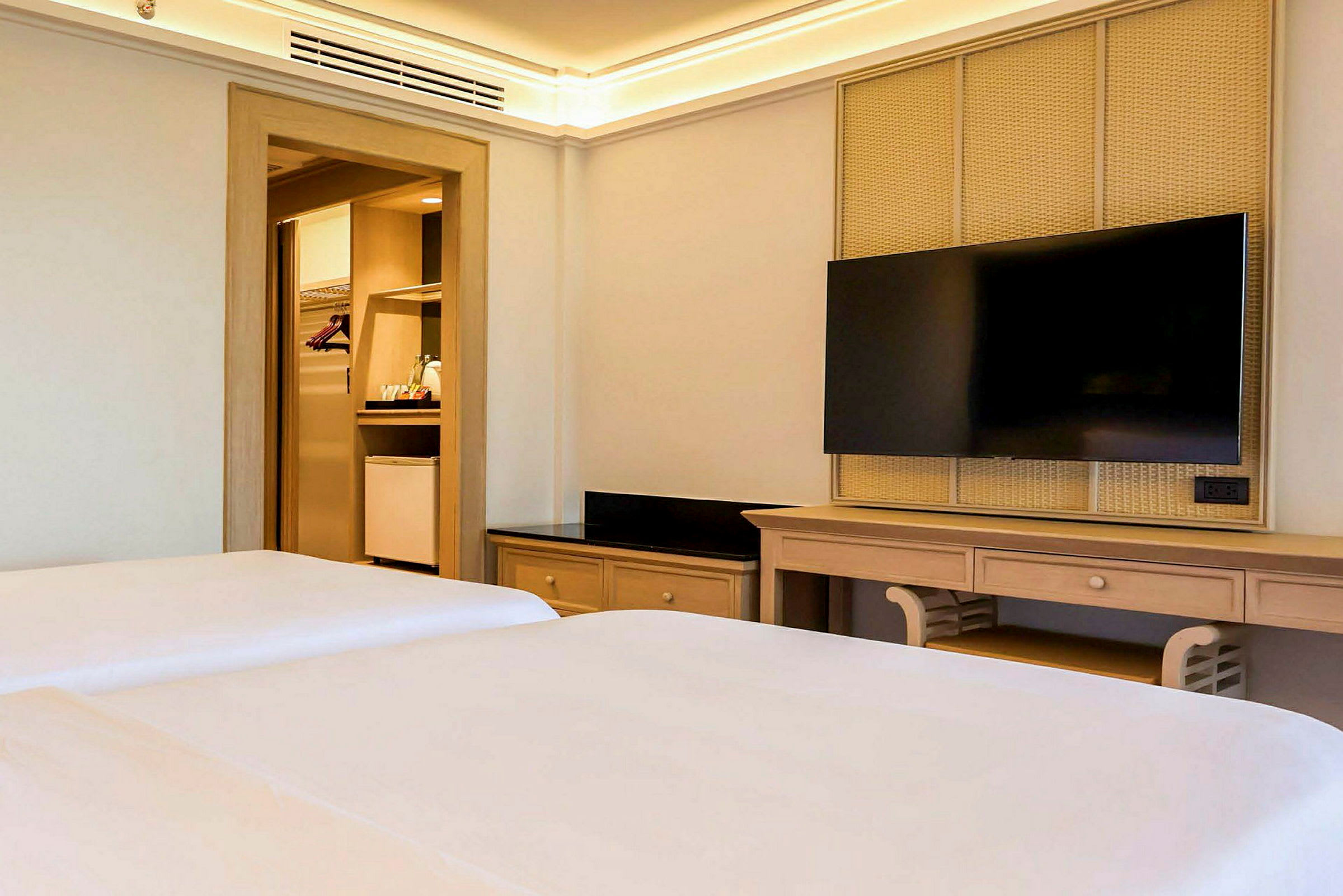Interiör av ett hotellrum med två sängar, en TV på väggen och en öppen garderob. (AI-genererad text)