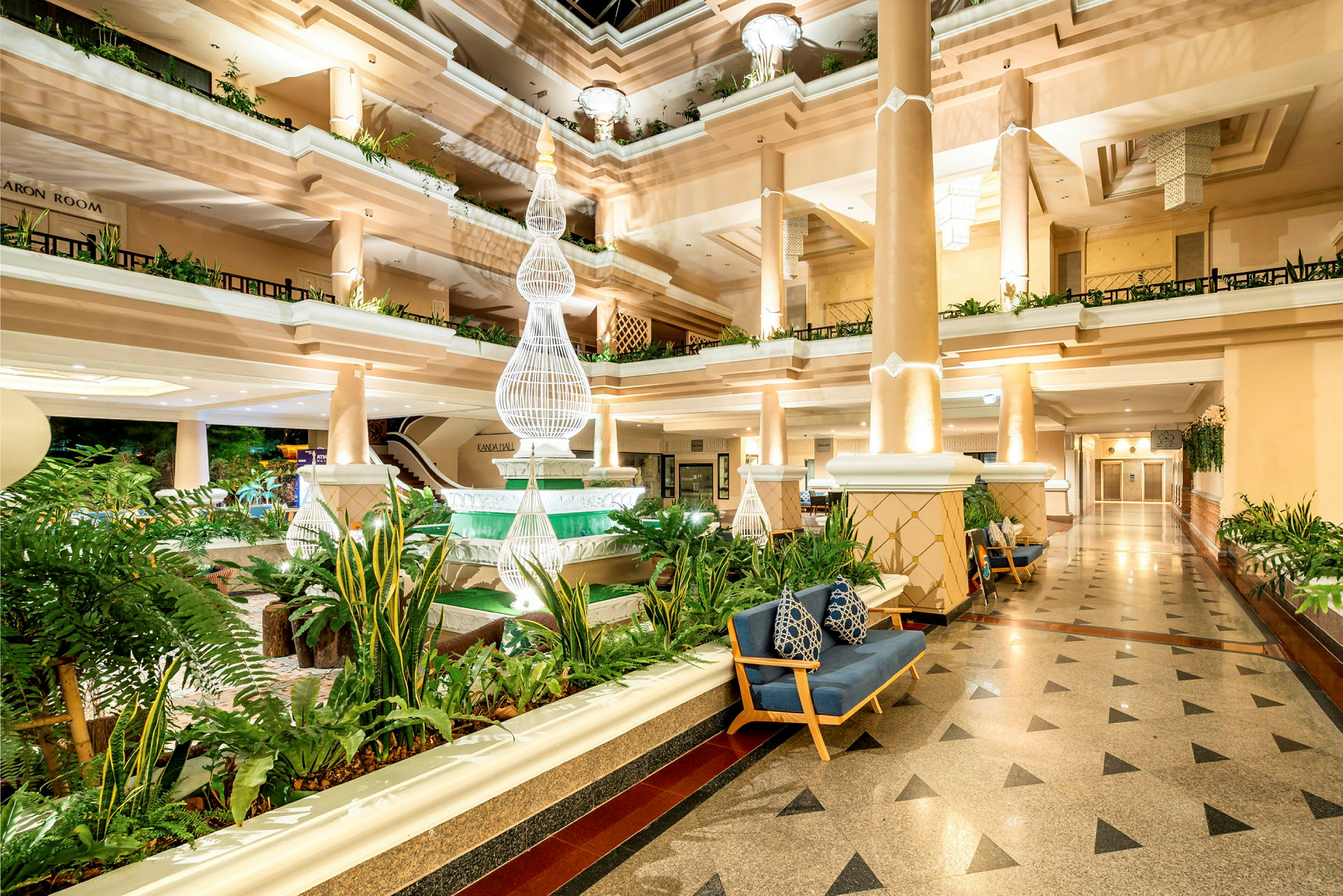 En ljus och elegant hotellobby med pelare, grönskande växter och dekorativ belysning. (AI-genererad text)
