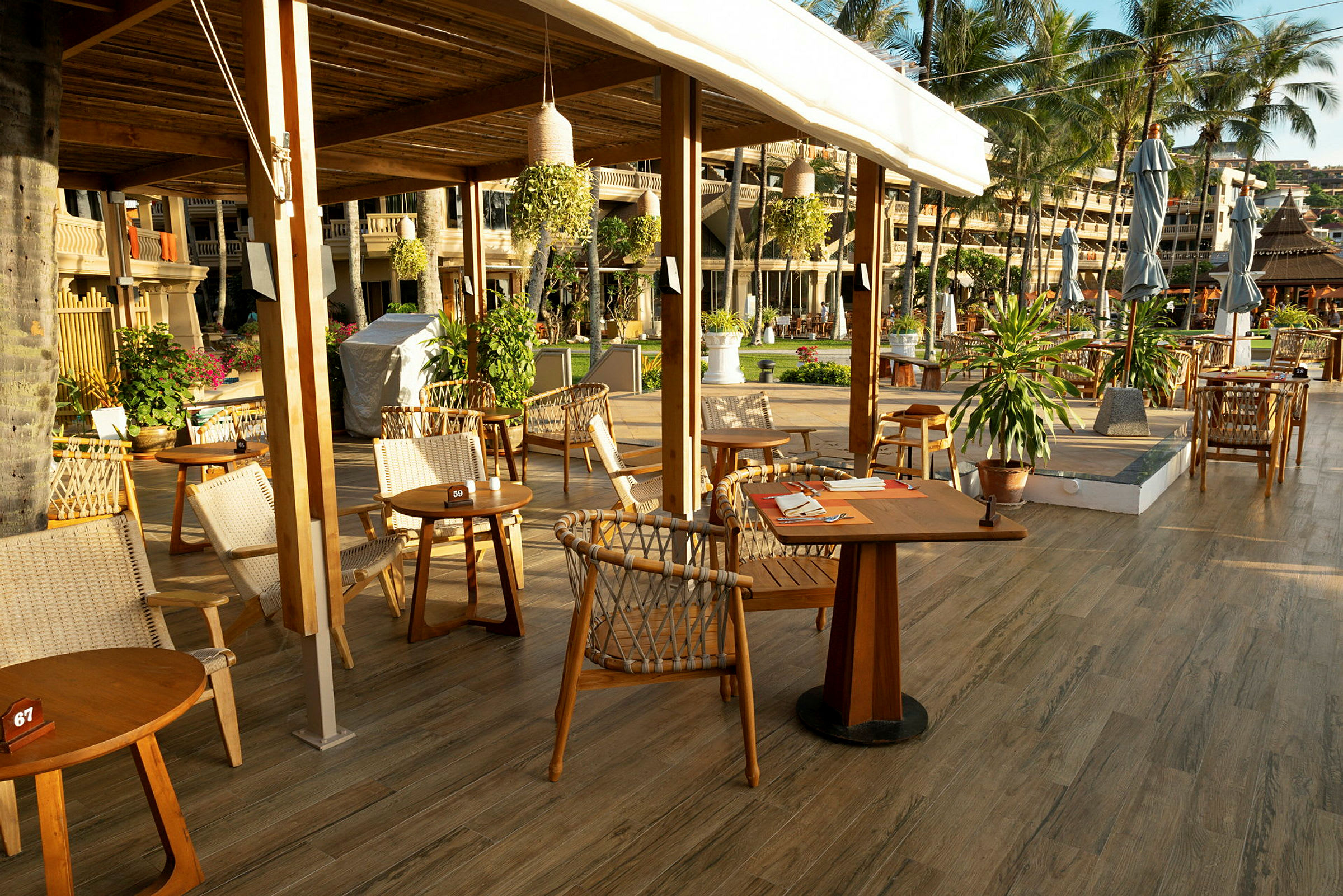 Outdoor restaurangområde med träbord och stolar, dekorerat med växter och beläget nära ett hotellområde. (AI-genererad text)