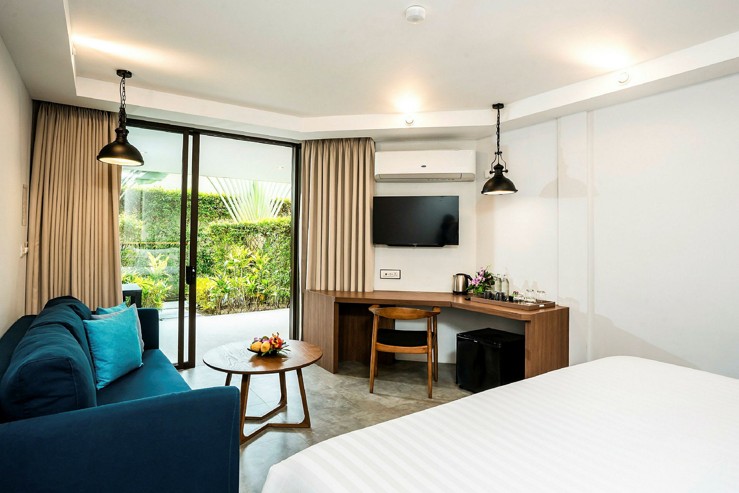 Ett hotellrum med soffa, bord, skrivbord, TV och glasdörrar mot en trädgård. (AI-genererad text)