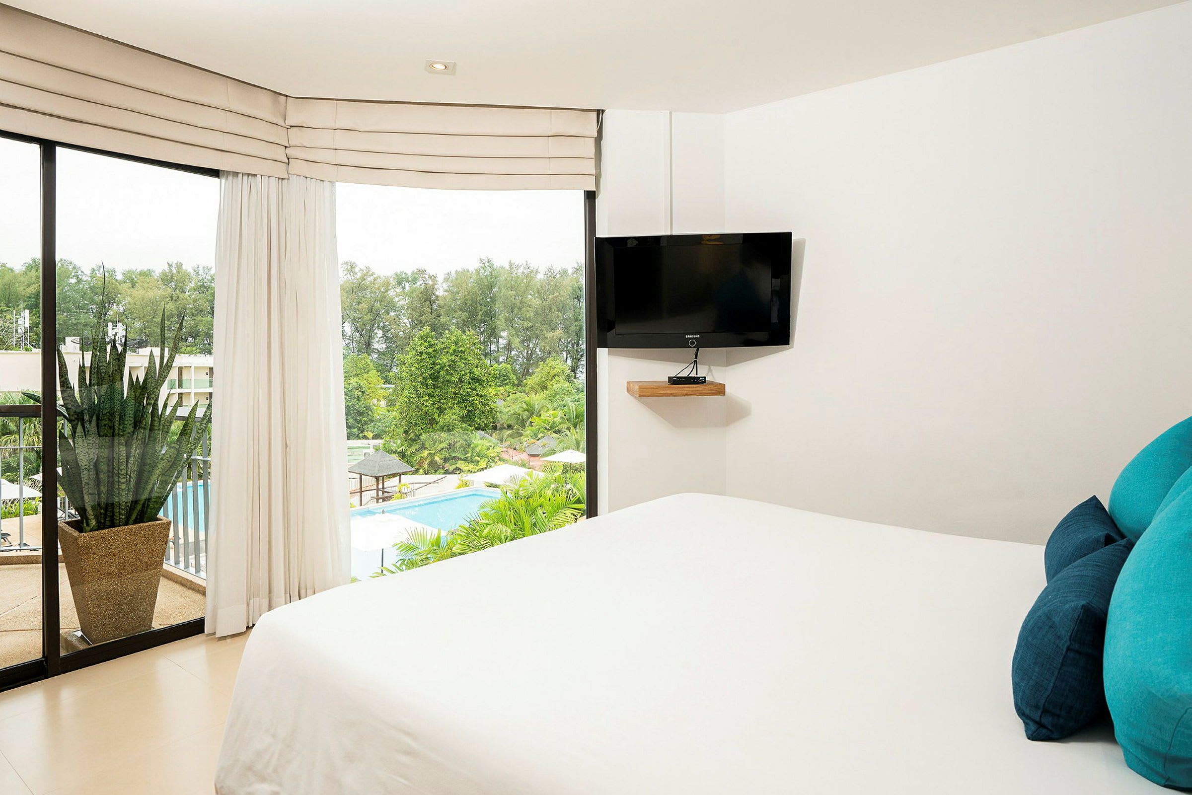Ett hotellrum med en säng och en TV vid väggen. Genom fönstret ser man en pool och grönska. (AI-genererad text)