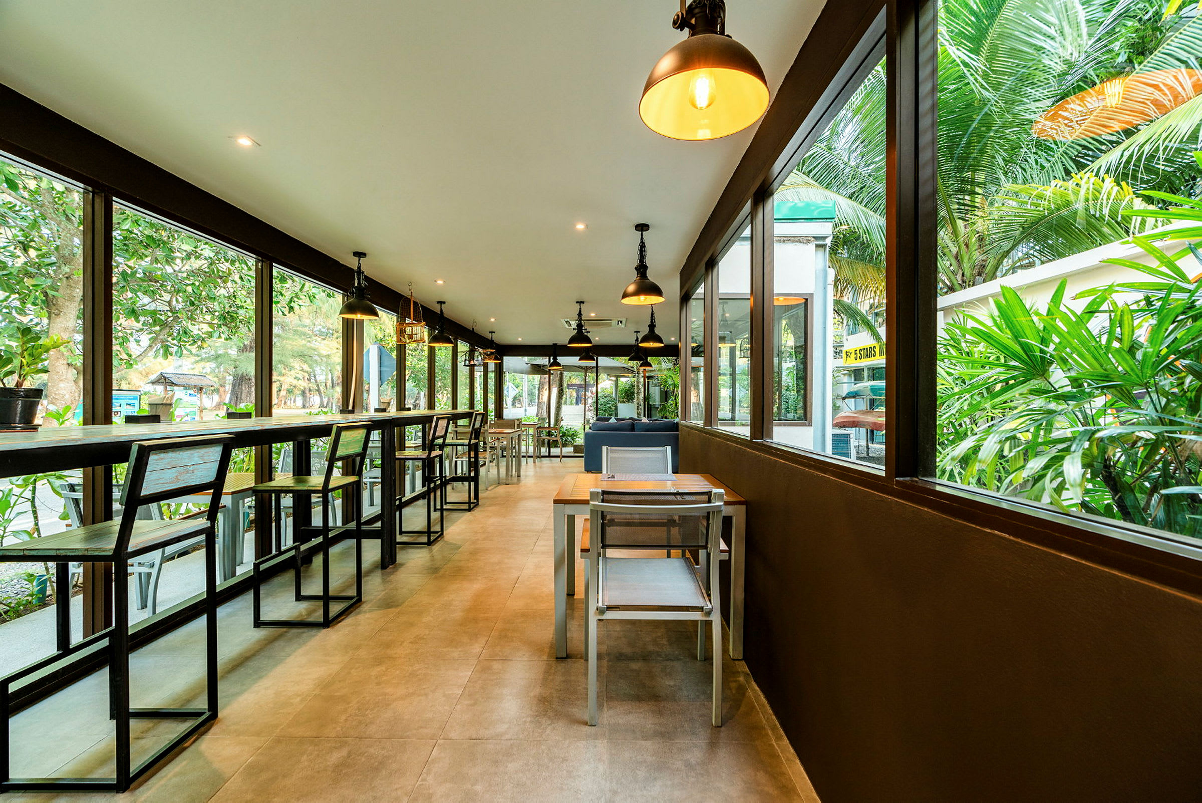 En modern restaurang med stora glasfönster och utsikt över grönska. (AI-genererad text)
