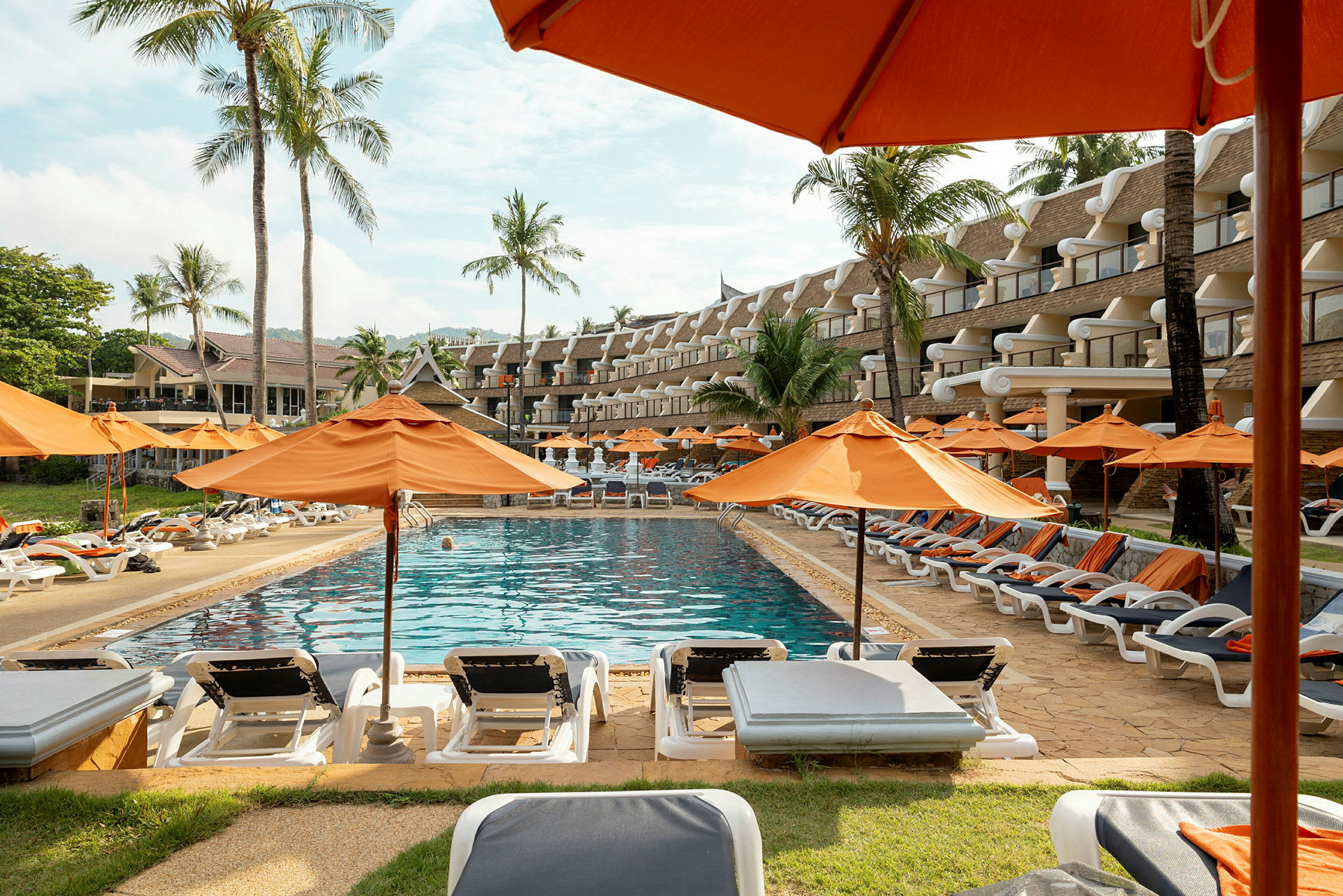 Pool med solstolar och orange parasoller, omgiven av palmer och hotellbyggnad. (AI-genererad text)
