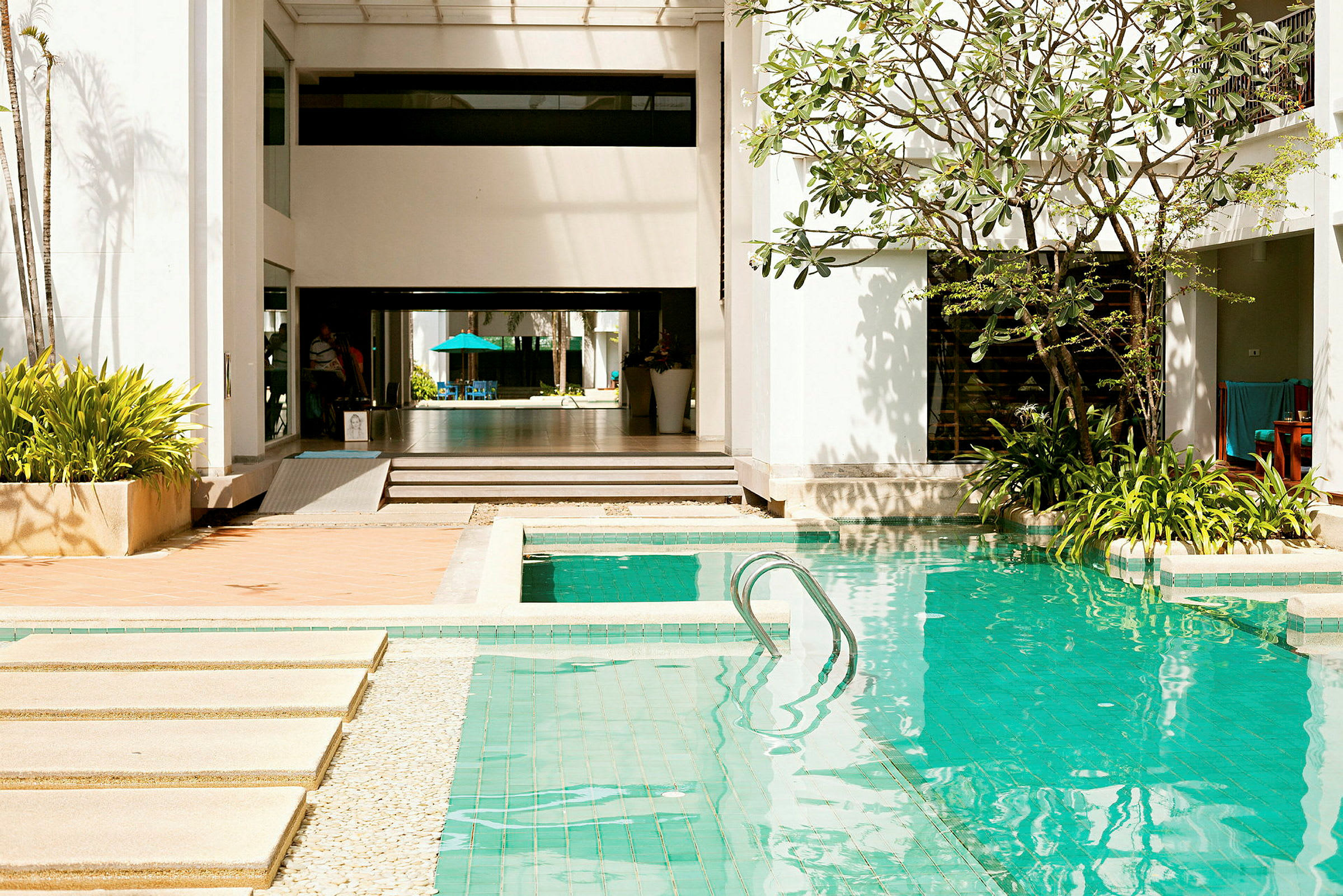 En utomhuspool omgiven av grönska och byggnader under dagsljus. (AI-genererad text)