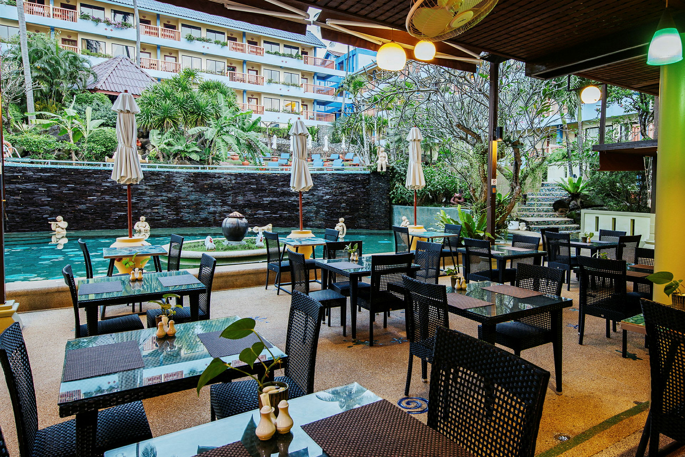 En öppen restaurang med bord och stolar vid en vacker fontän och pool. (AI-genererad text)