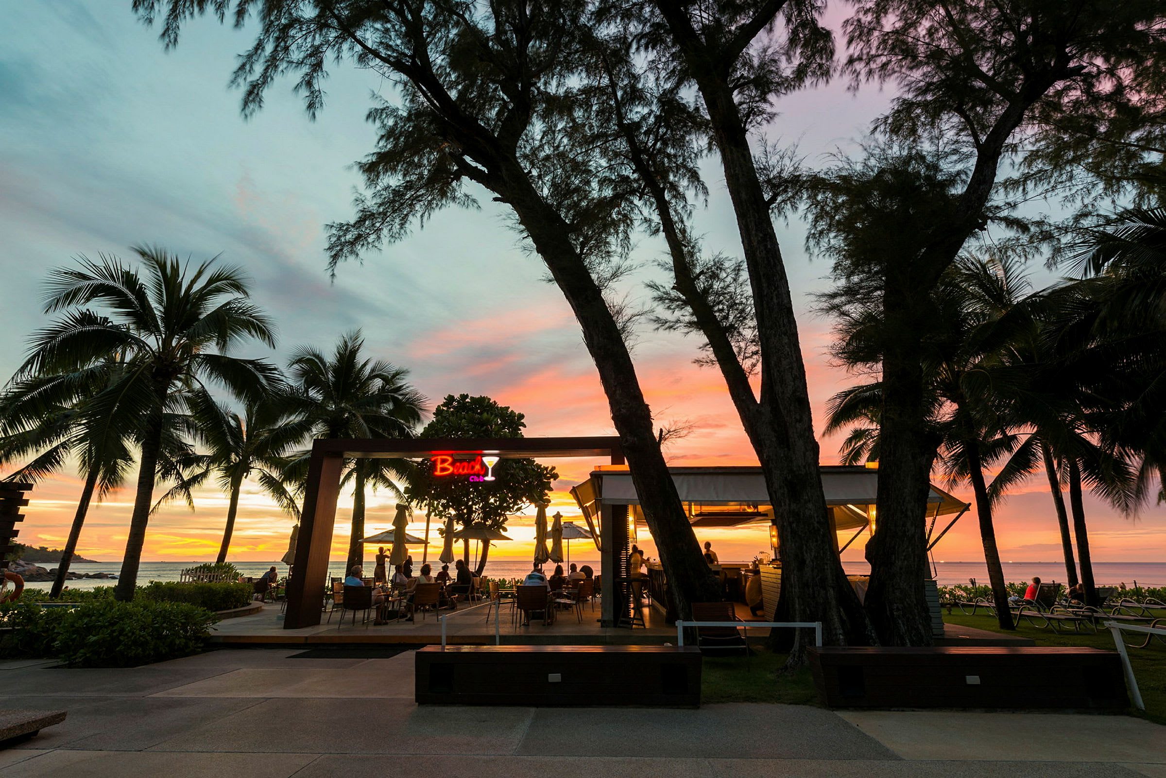 En strandbar med utsikt över havet vid solnedgången, omgiven av palmer. (AI-genererad text)
