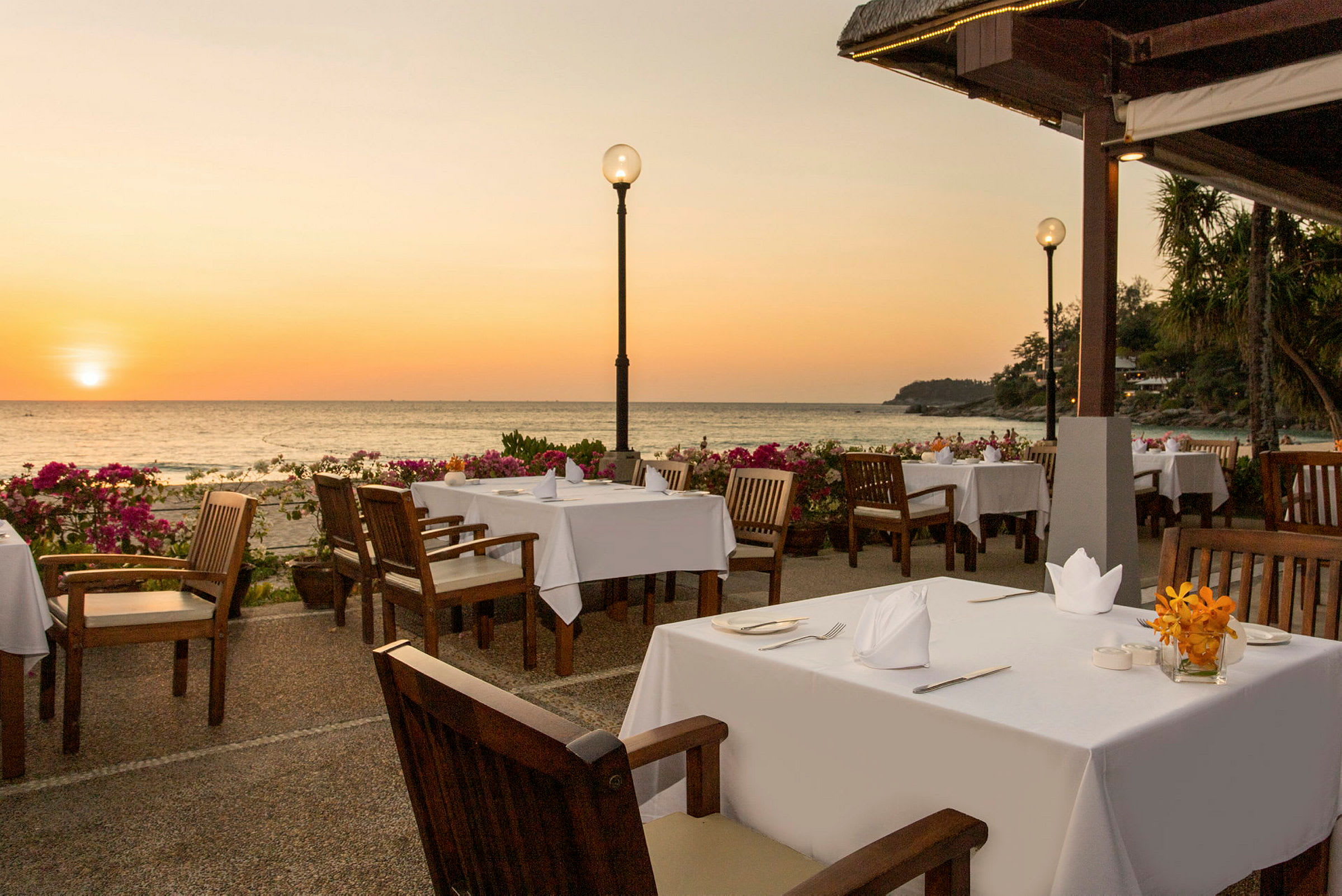 Utomhusrestaurang med dukade bord nära havet i solnedgången. (AI-genererad text)