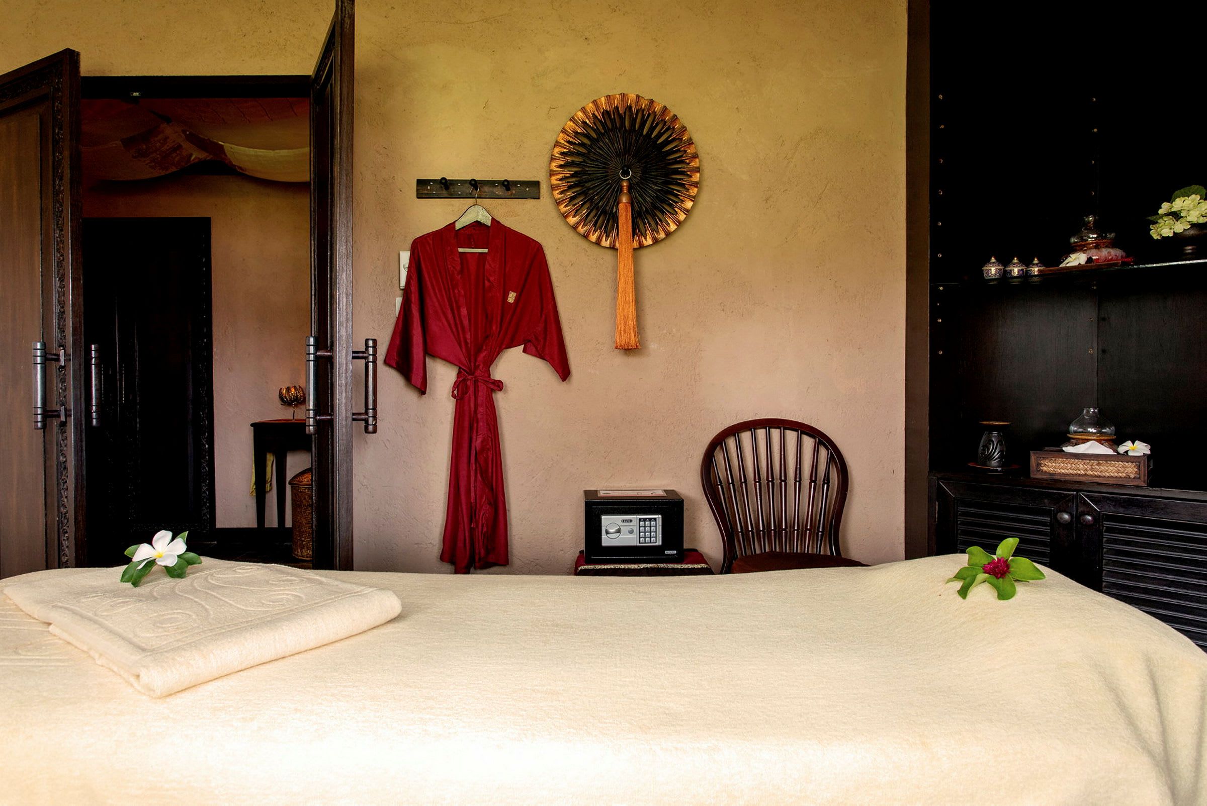 Ett spa-rum med massagebänk, röd badrock och dekorativ väggprydnad. (AI-genererad text)