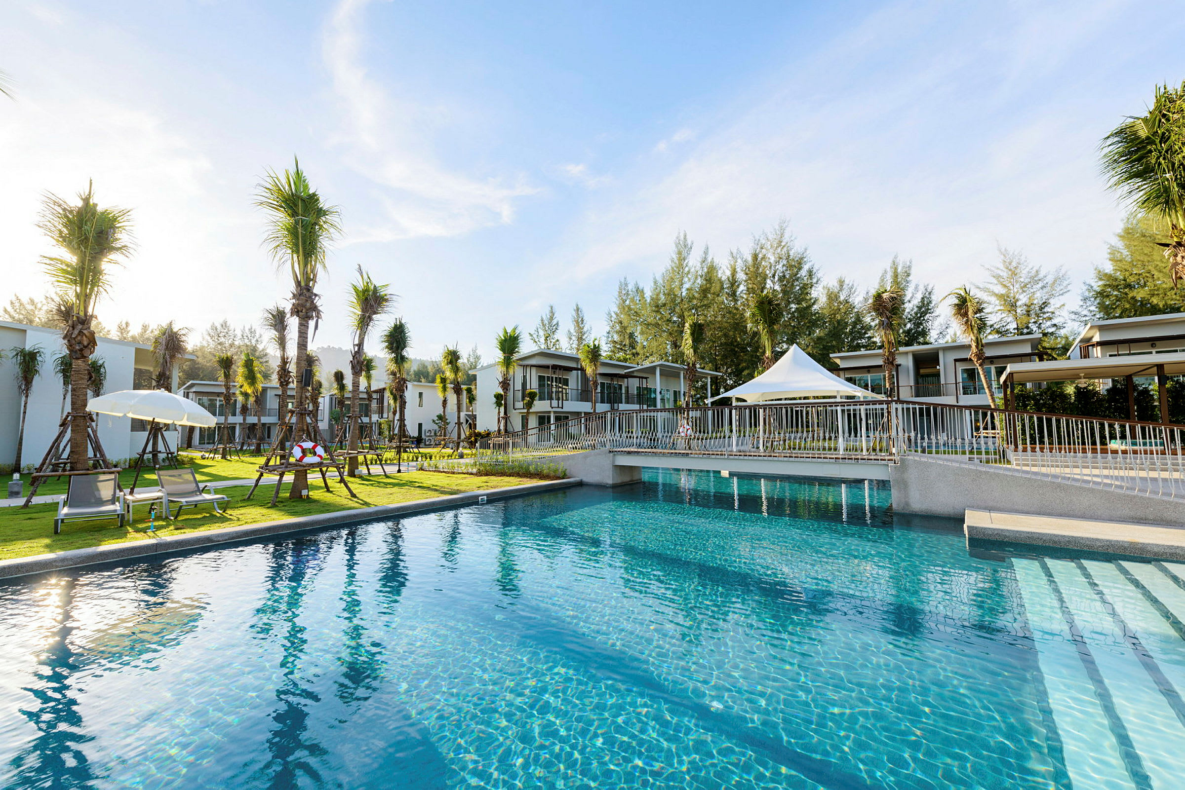 Utemiljö med pool, solstolar, träd och moderna byggnader i bakgrunden. (AI-genererad text)