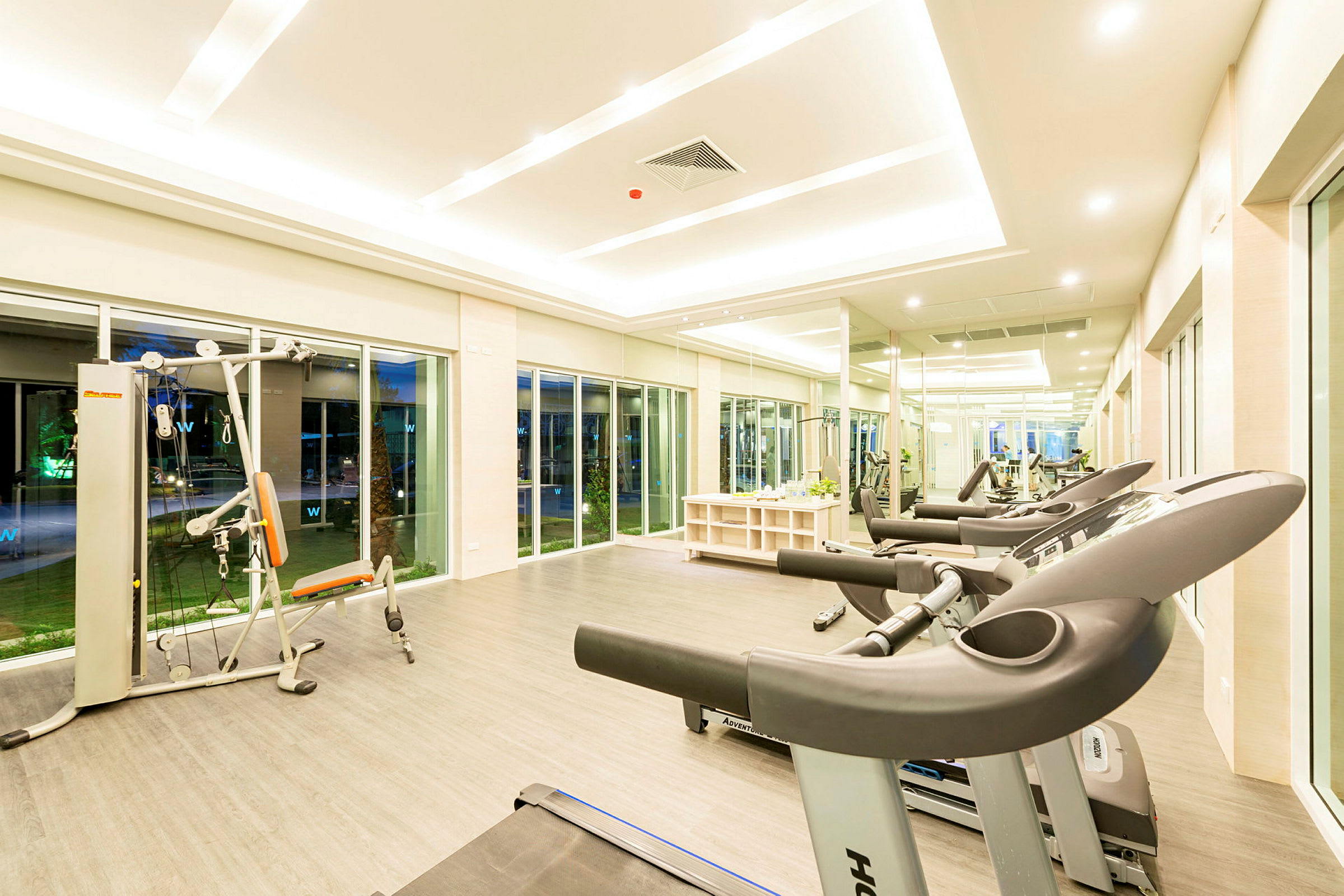 Ett gym med träningsmaskiner, löpband och stora fönster. (AI-genererad text)