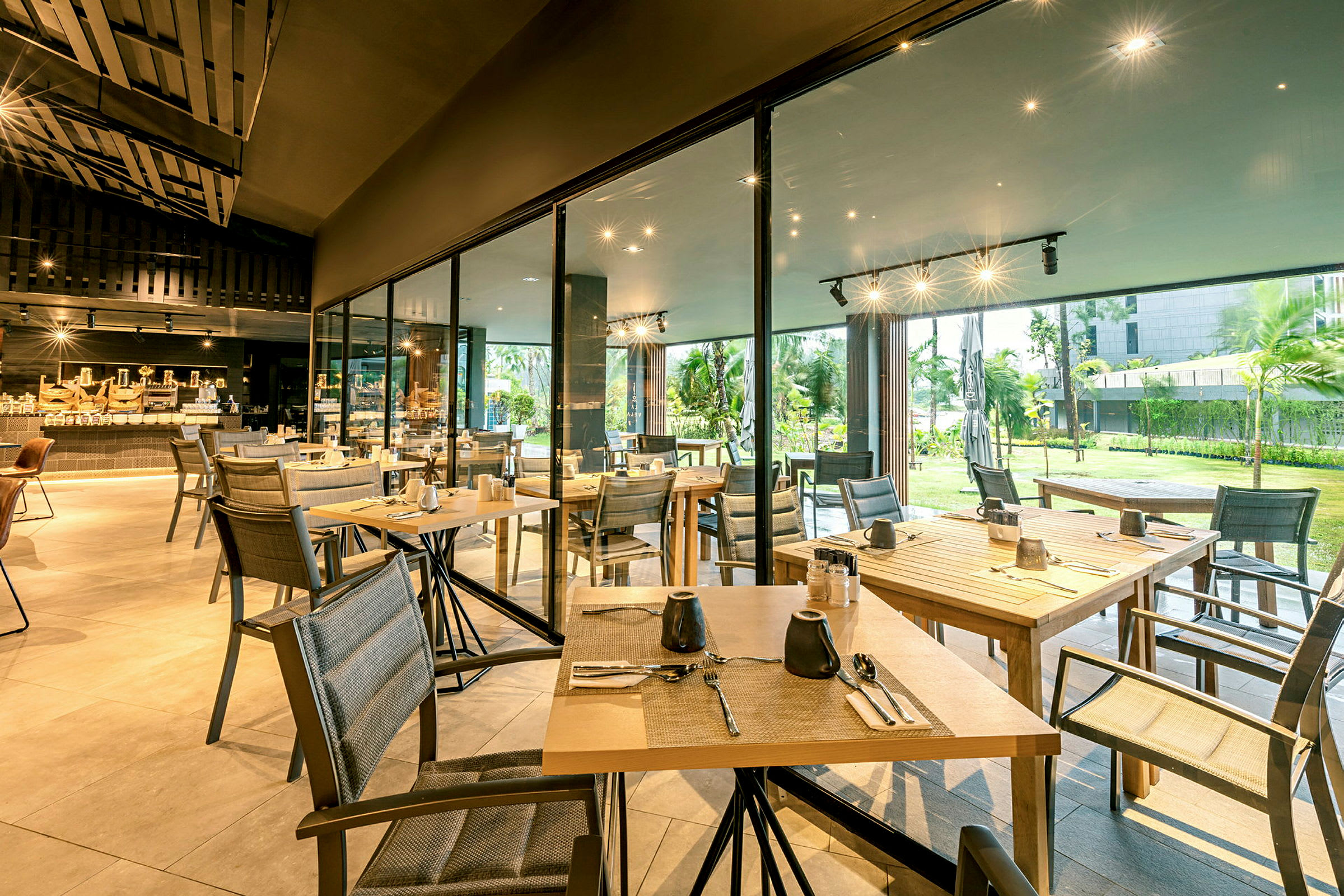 En restaurang med träbord och stolar, belägen nära ett fönster med utsikt över en grönskande trädgård. (AI-genererad text)