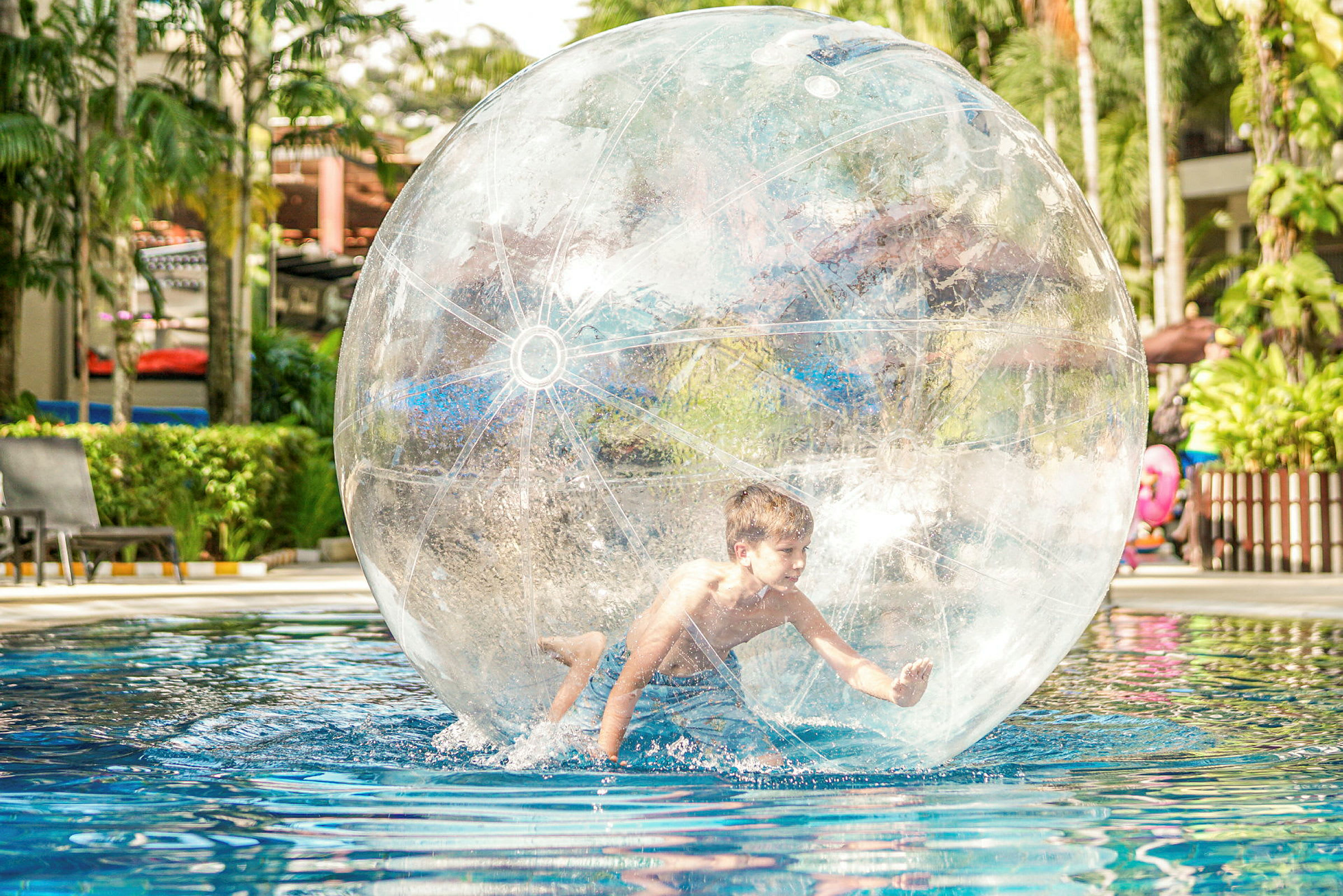 Person inuti en genomskinlig uppblåsbar boll flytande i en pool omgiven av grönska. (AI-genererad text)