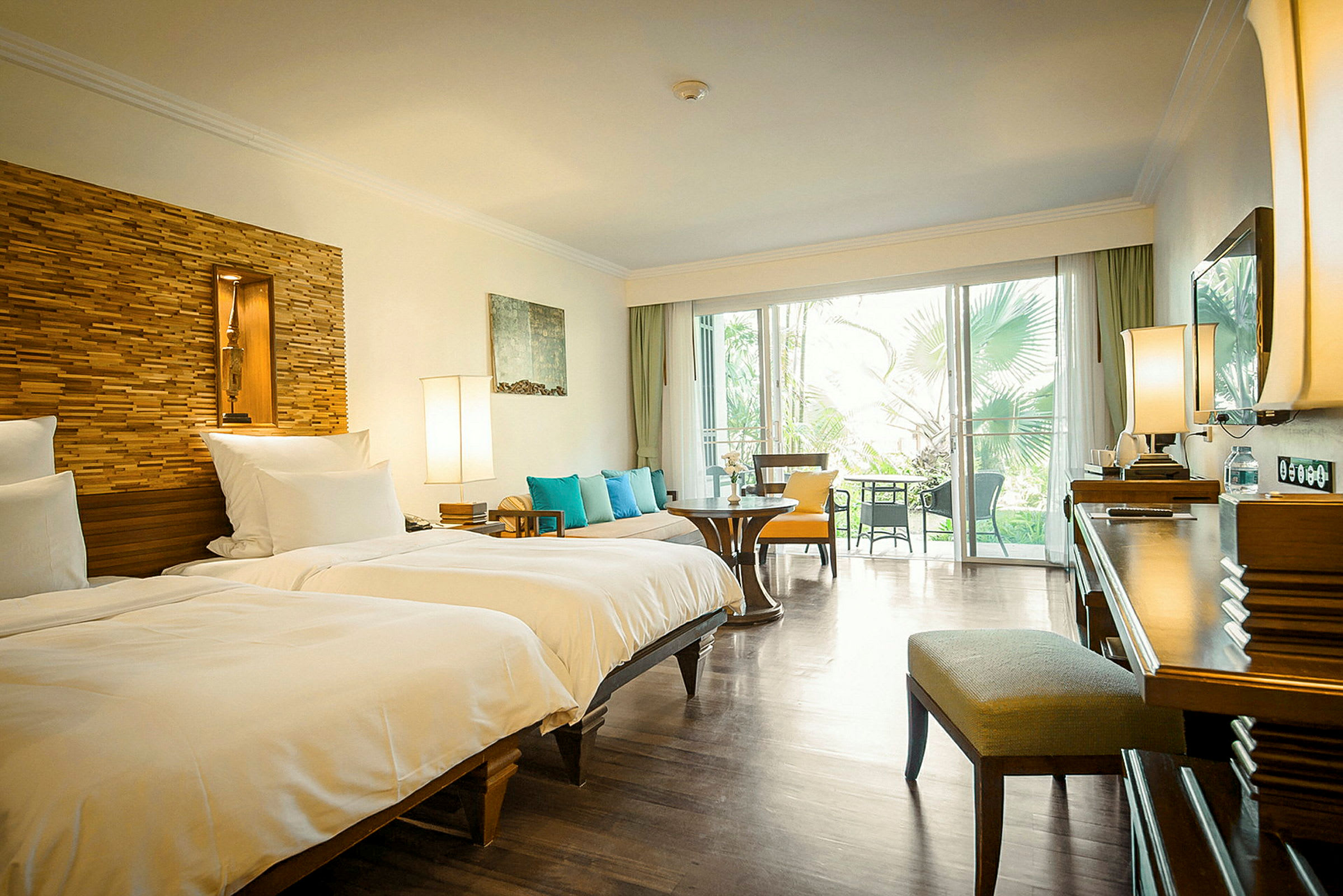 Hotellrum med två enkelsängar, sittplats och utsikt mot en grönskande utomhusmiljö. (AI-genererad text)