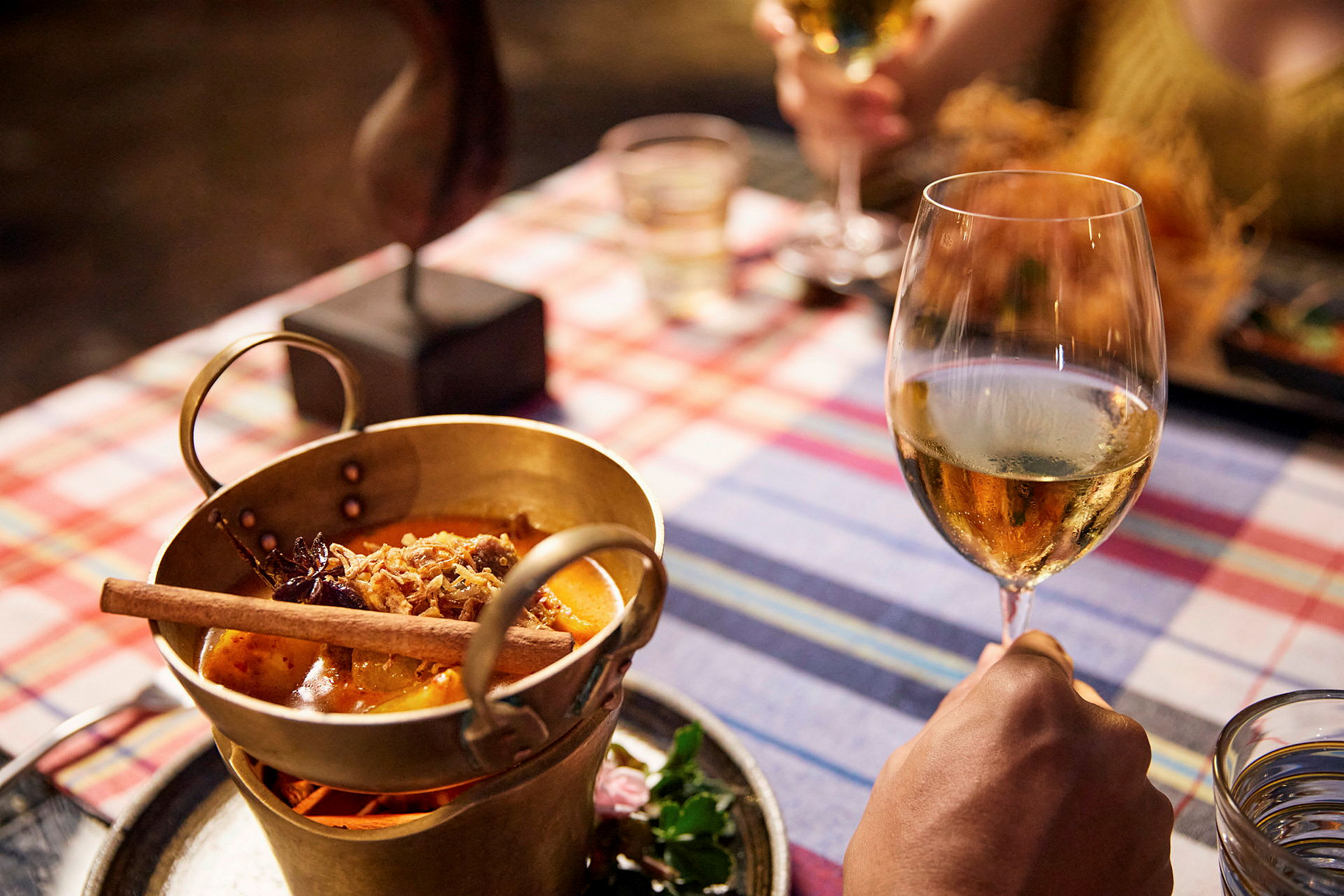 Ett mässingskärl med mat samt ett glas vitt vin på ett dukat bord. (AI-genererad text)