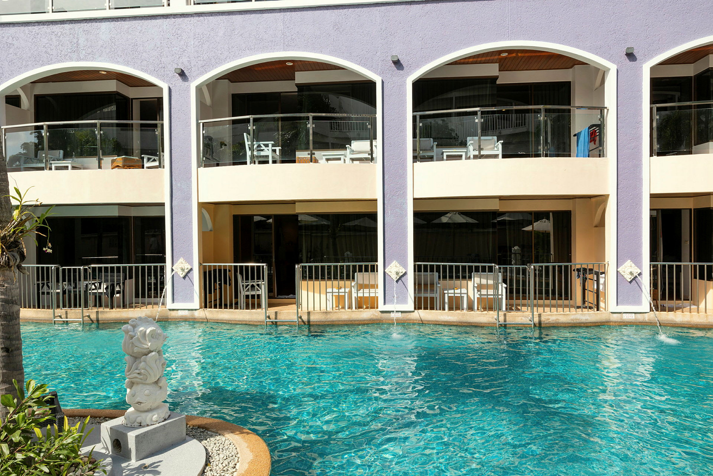 Hotellfasad med balkonger ovanför poolen. (AI-genererad text)