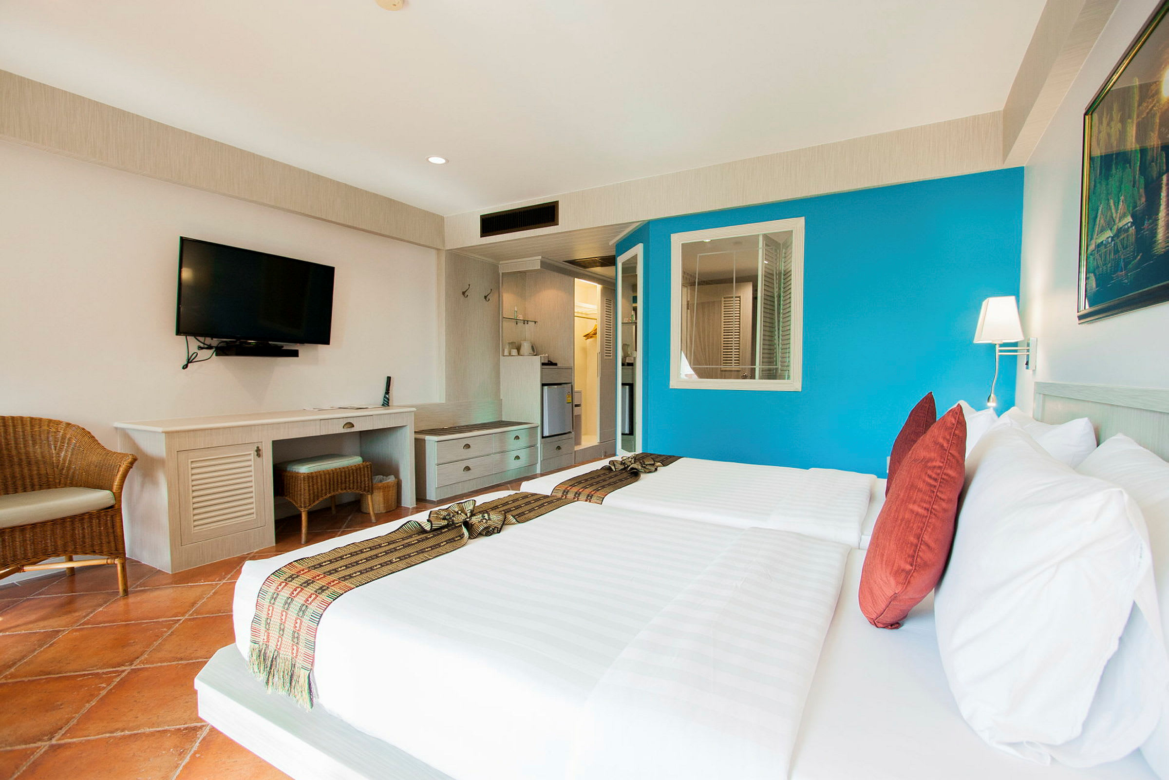 Hotellrum med två bäddar, blå vägg, TV på väggen och skrivbord. (AI-genererad text)