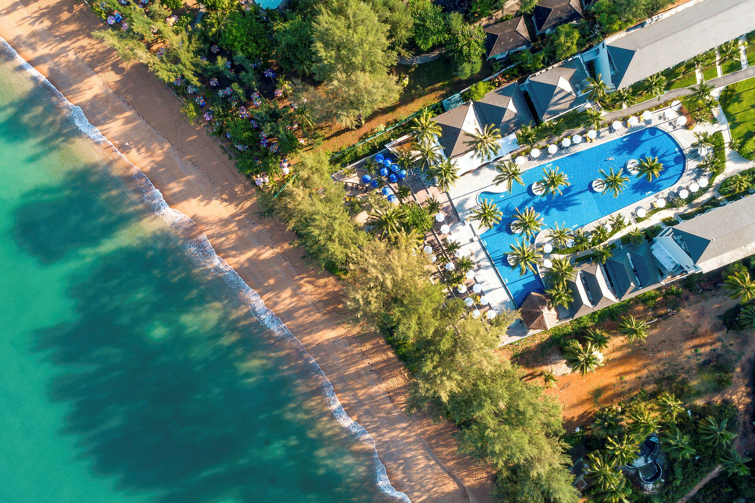 Flygbild av en strand bredvid ett hotellområde med en pool. (AI-genererad text)