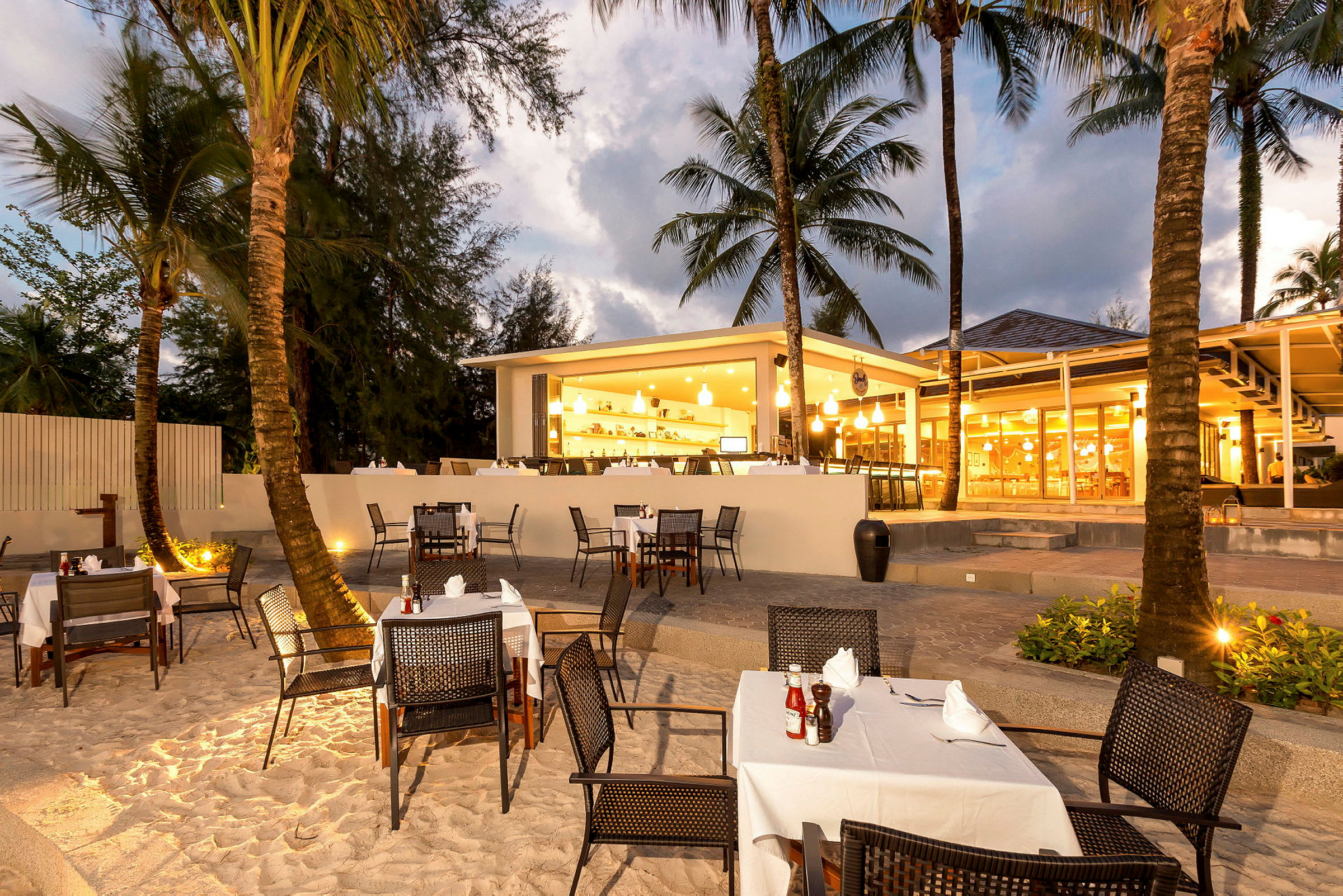 Restaurang med uteservering vid stranden, omgiven av palmträd. (AI-genererad text)