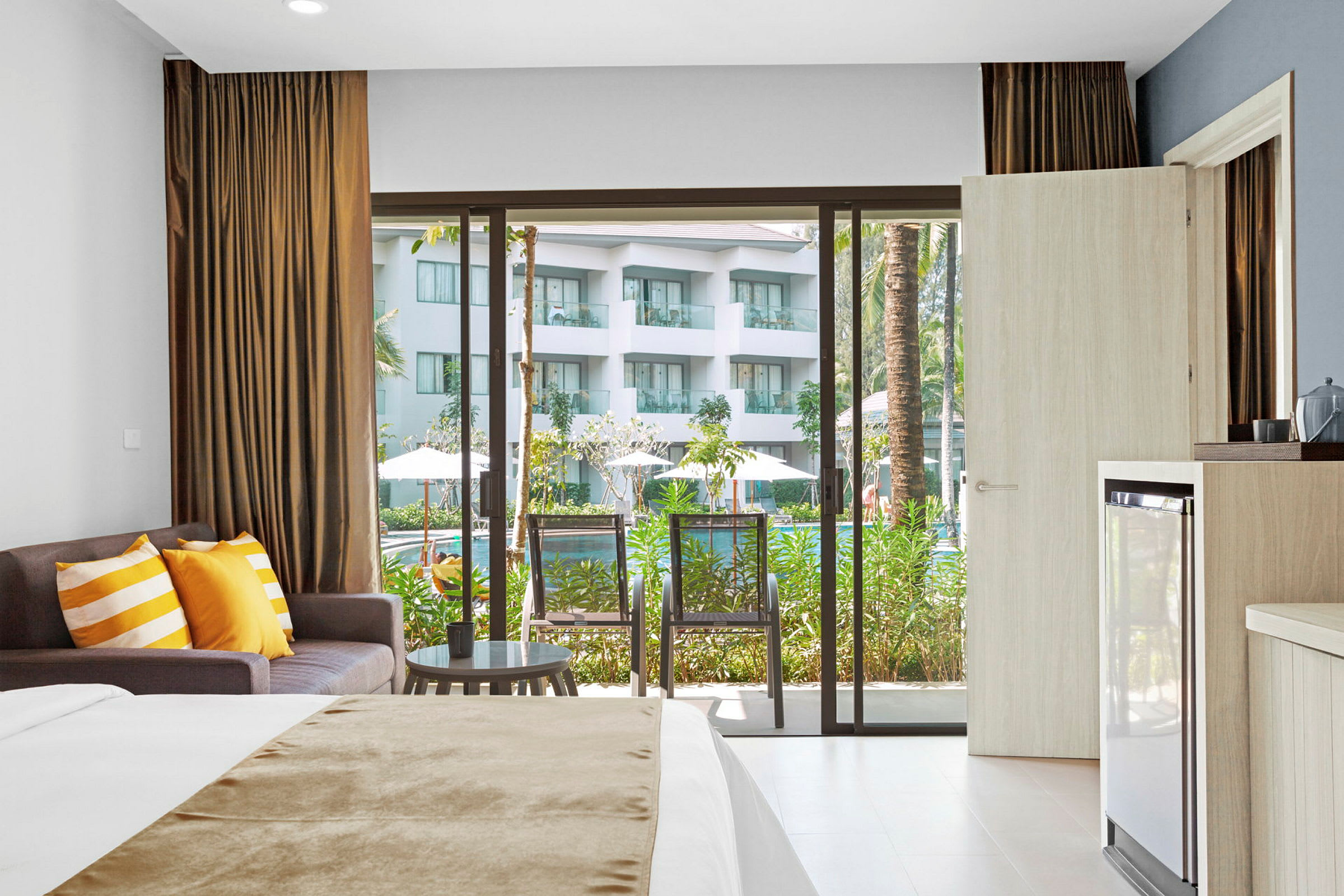 Hotellrum med säng, soffa och balkong med utsikt mot poolområde. (AI-genererad text)