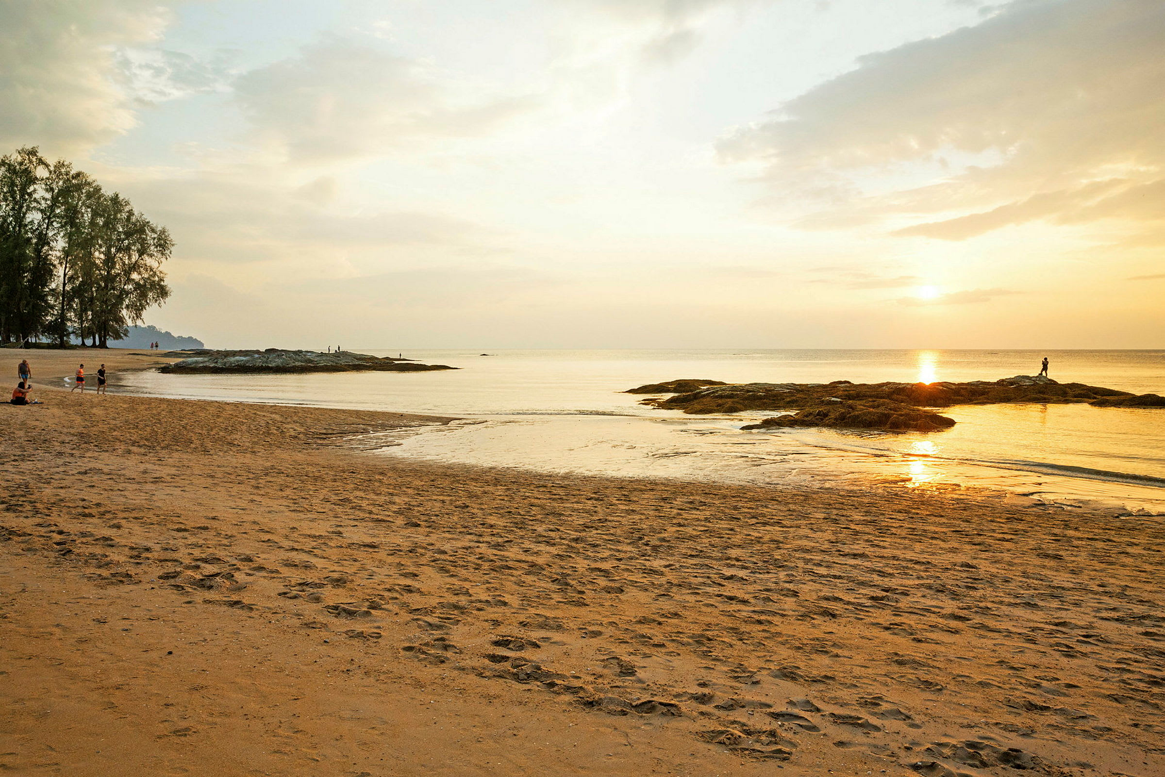 Solnedgång vid en lugn strand med några personer och klippor vid vattnet. (AI-genererad text)