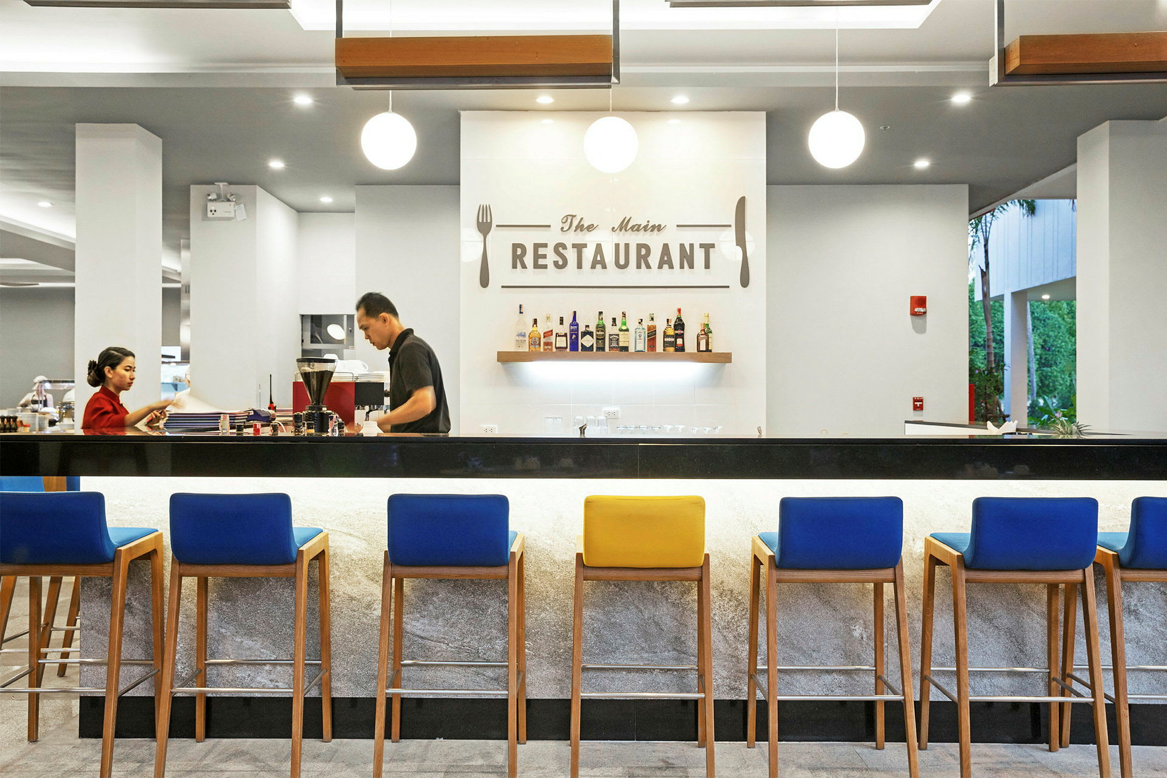 En elegant restaurang med en modern inredning, en bar med färgglada stolar och en vägg med upphängda flaskor och en skylt med texten 'The Main Restaurant'. (AI-genererad text)