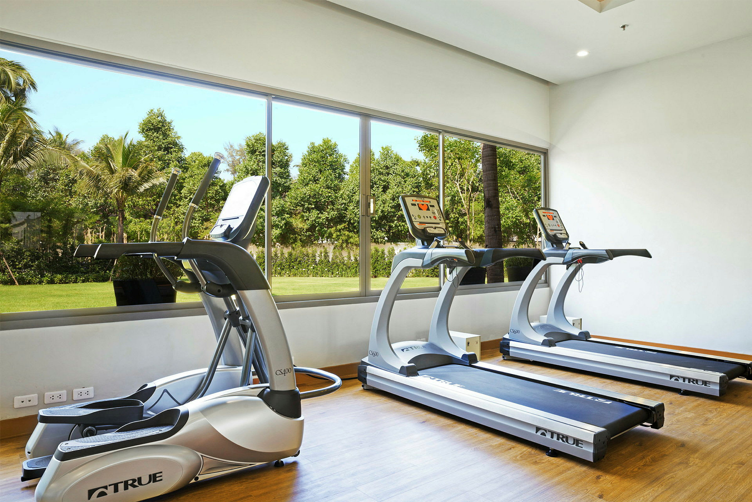 Ett gym med träningsmaskiner bredvid ett stort fönster med utsikt över en grön utomhusmiljö. (AI-genererad text)
