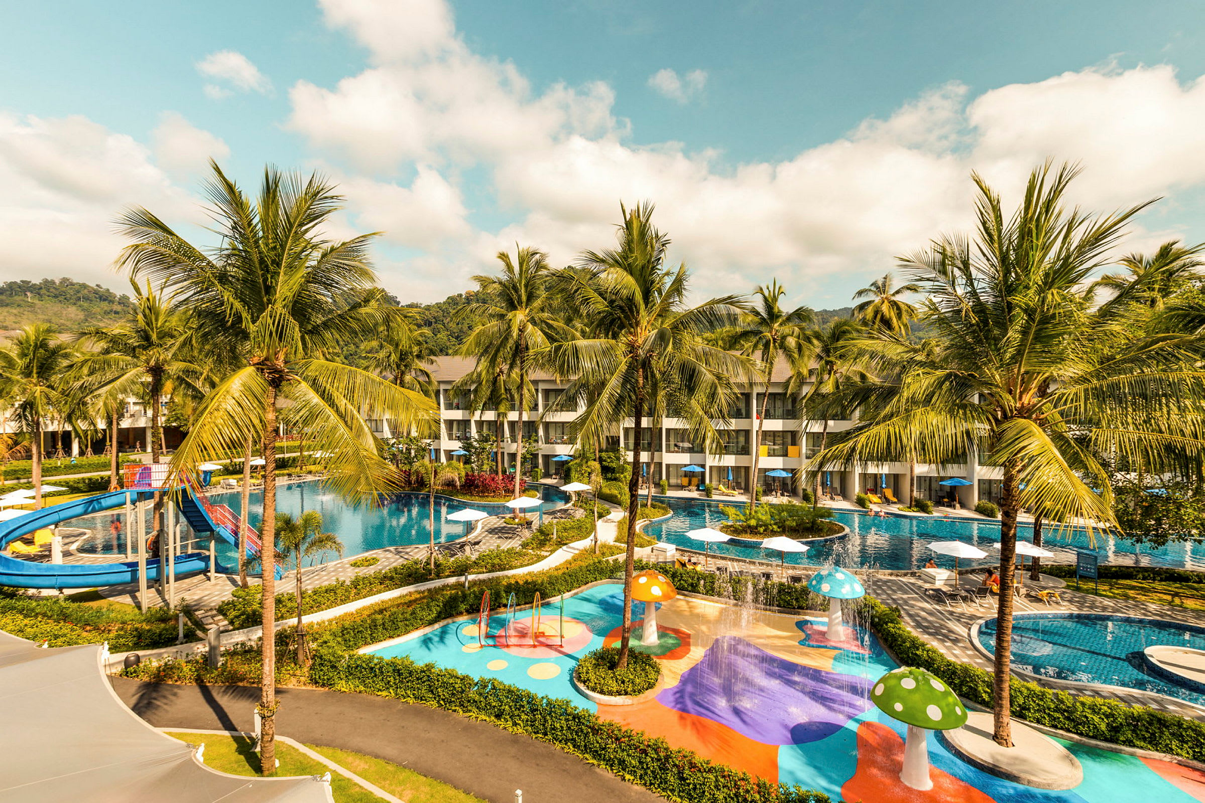 Bild av ett hotellområde med pooler, vattenrutschbana och färgglada lekområden omgiven av palmträd. (AI-genererad text)