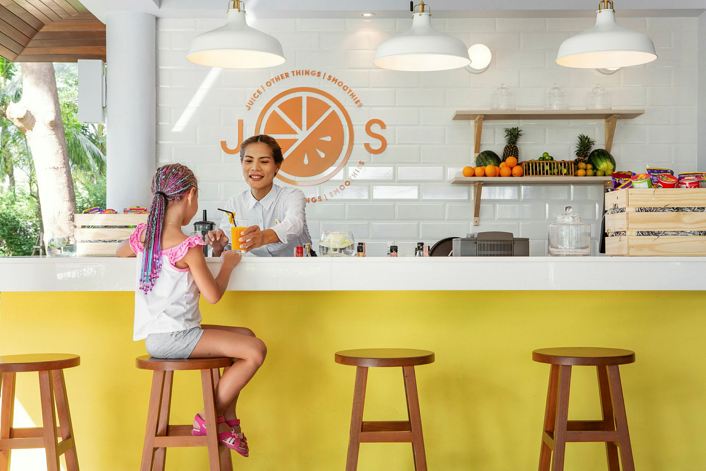 En flicka sitter vid en juicebar som har färska frukter och snacks på hyllan. (AI-genererad text)