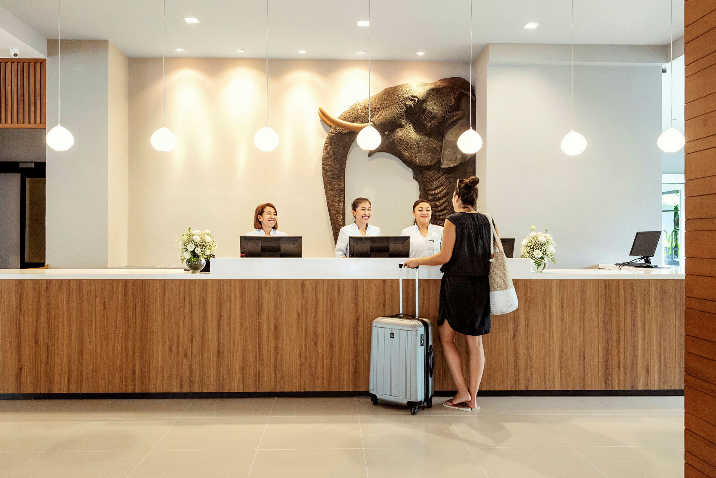 En kvinna står vid en hotellreception med en resväska. (AI-genererad text)
