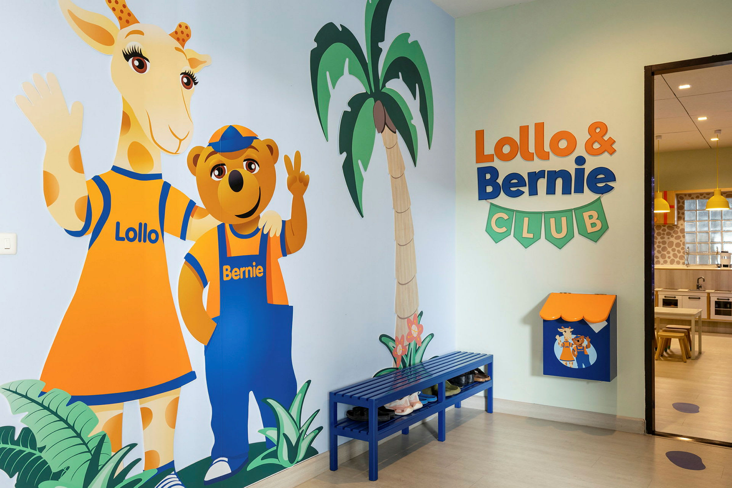 En färgglad väggmålning av figurerna Lollo och Bernie står vid en vägg i en barnklubb. Rummet har också en blå bänk och skyltar. (AI-genererad text)