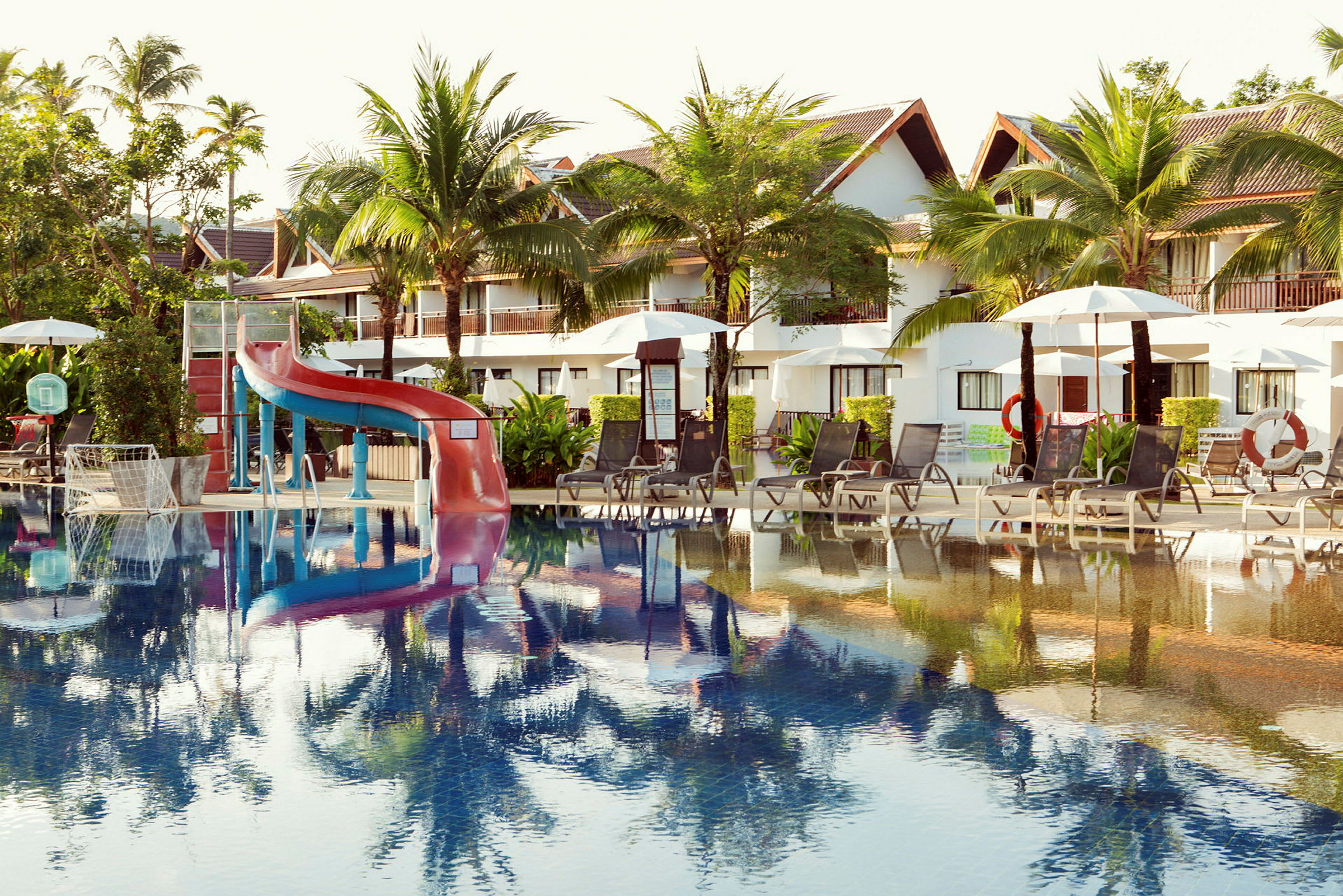 Bild av en utomhuspool vid en resort med solstolar, parasoller och en vattenrutschkana. (AI-genererad text)