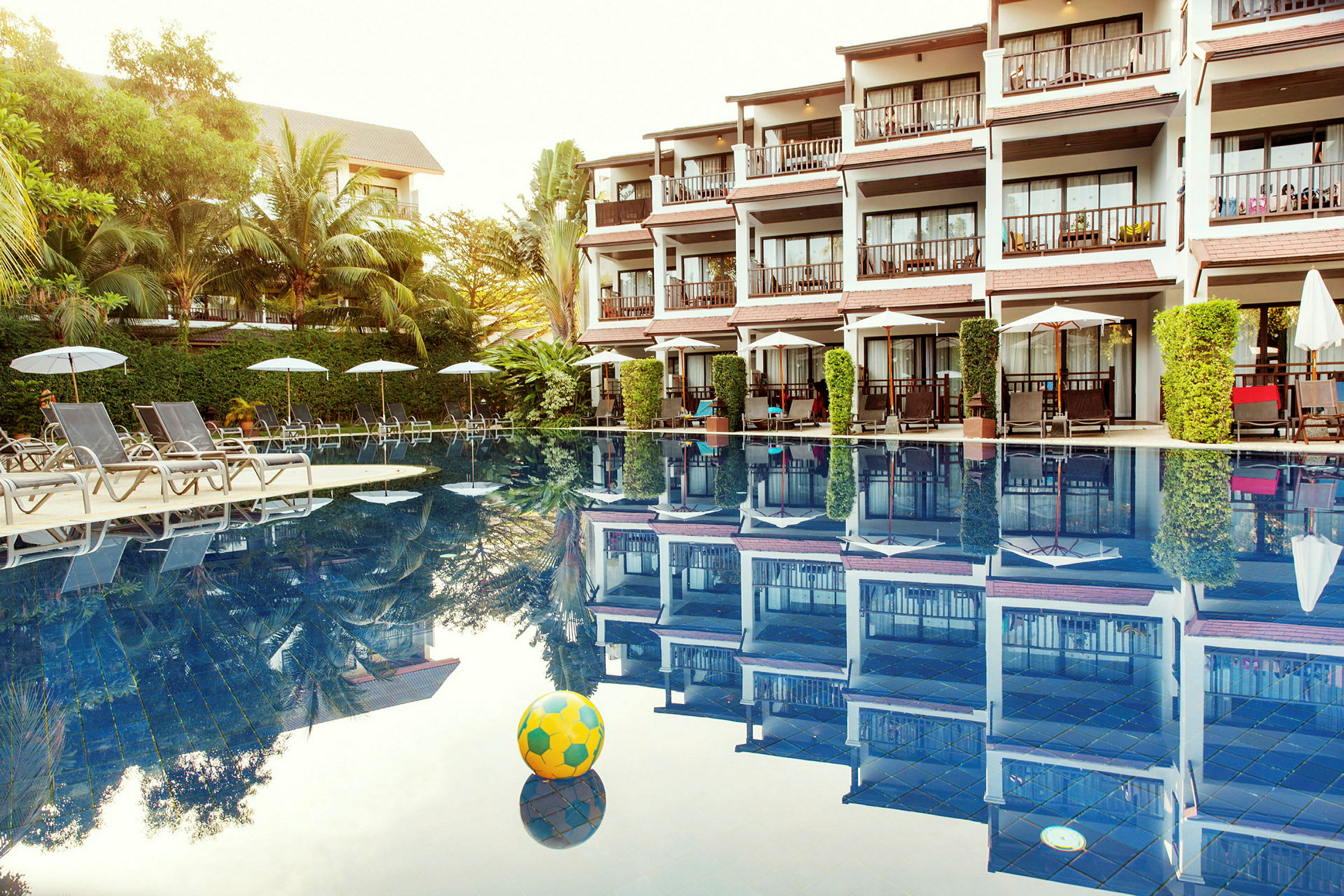 Hotell med flera balkonger vid en pool med solstolar och parasoller. (AI-genererad text)