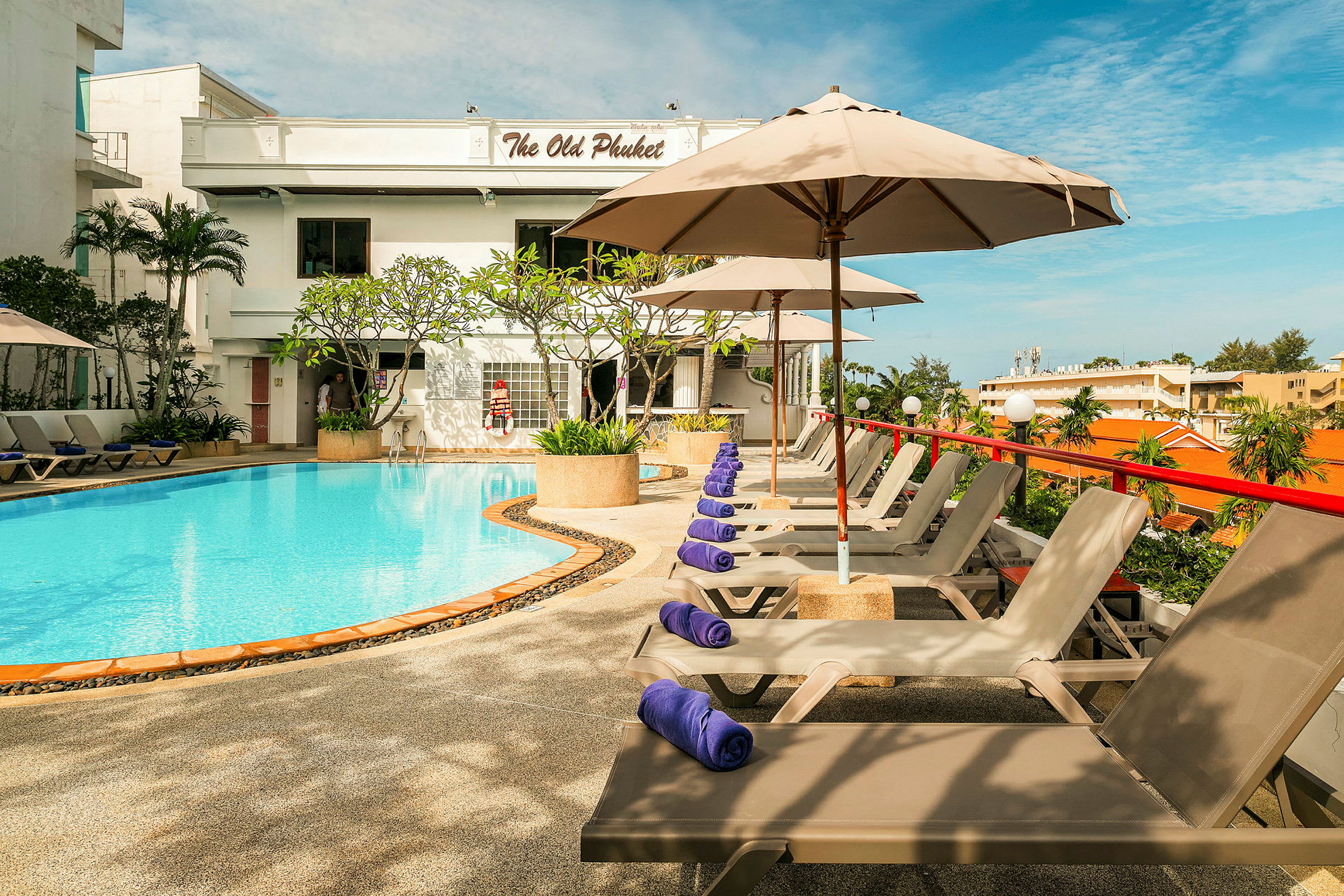 En utomhuspool med solstolar och parasoller vid en byggnad med texten 'The Old Phuket'. (AI-genererad text)