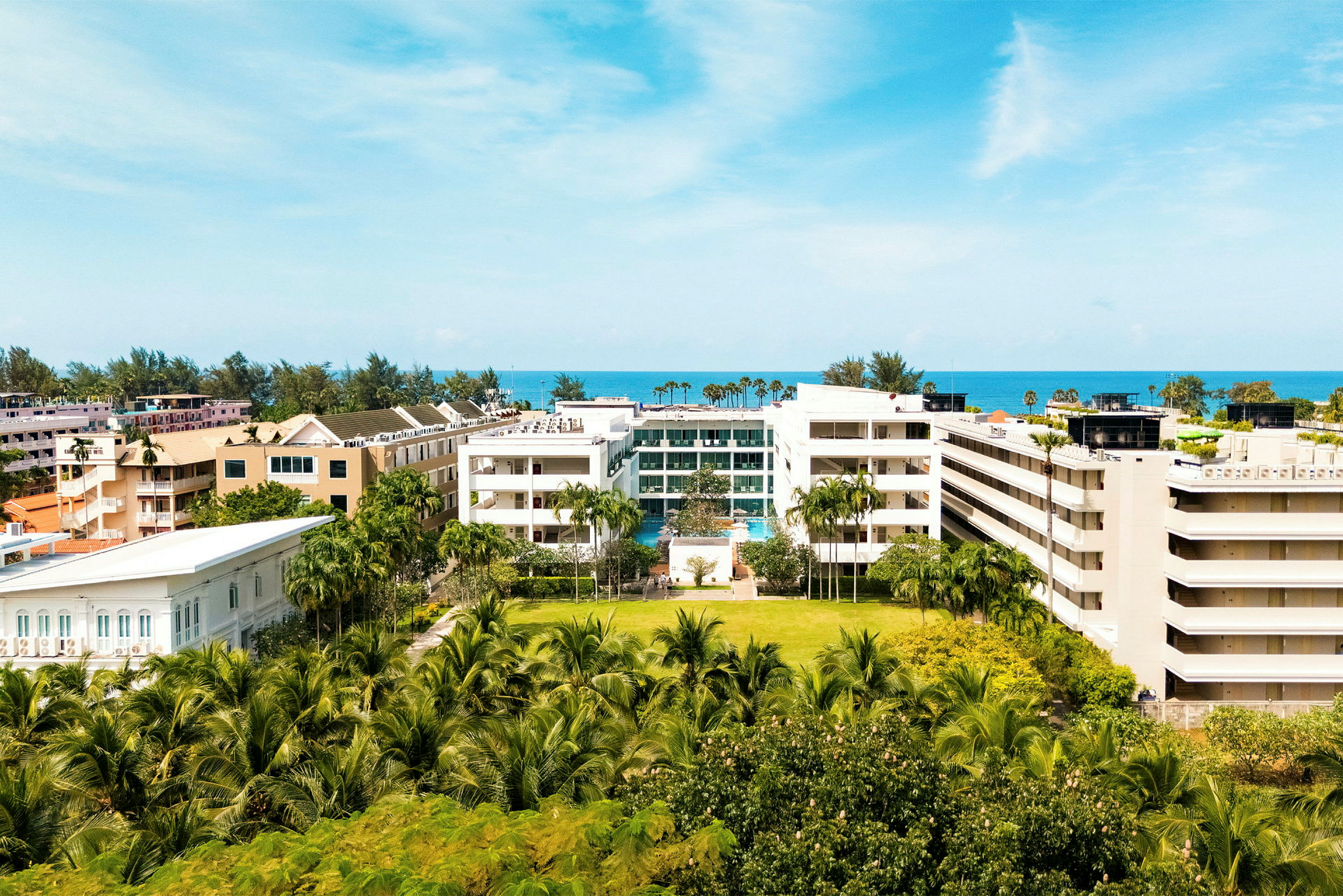 Vy över ett semesterområde nära havet med hotellkomplex och frodig växtlighet. (AI-genererad text)