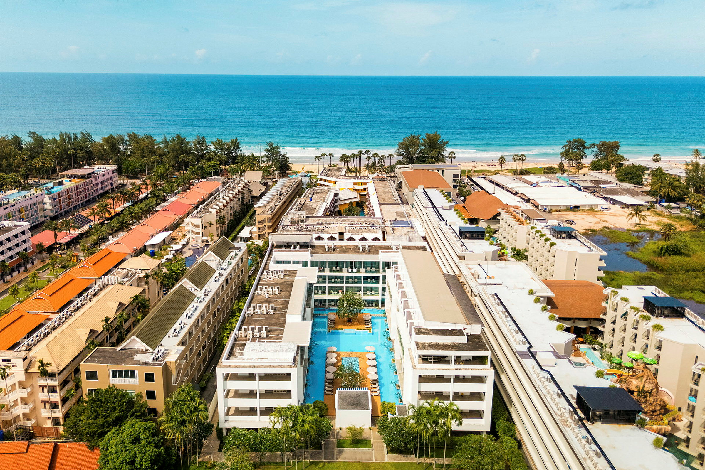 En hotellbyggnad med en pool i mitten, omgiven av fler byggnader nära havet. (AI-genererad text)