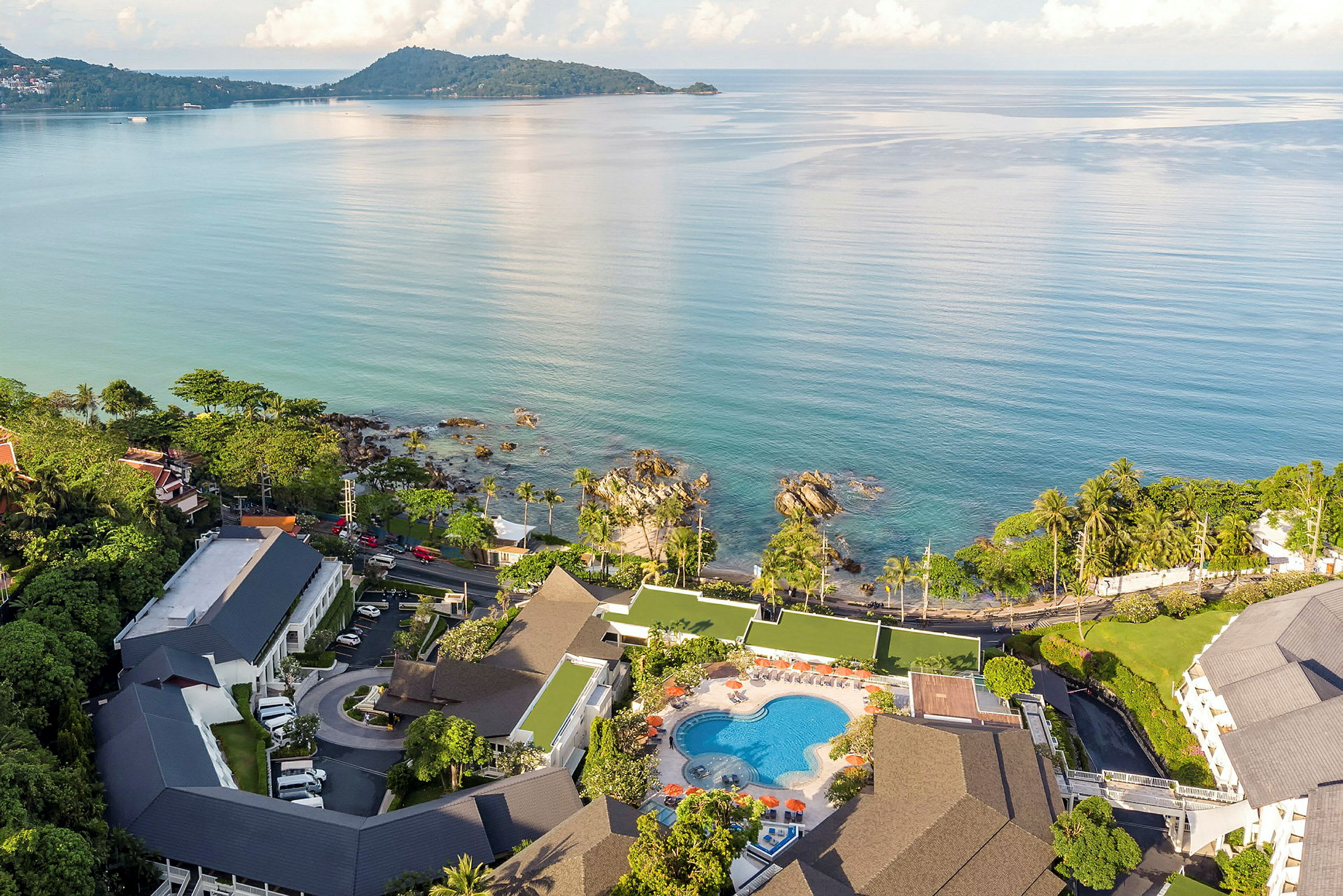 Flygfoto över en strandnära resort med poolområde och byggnader omgivna av grönska. (AI-genererad text)
