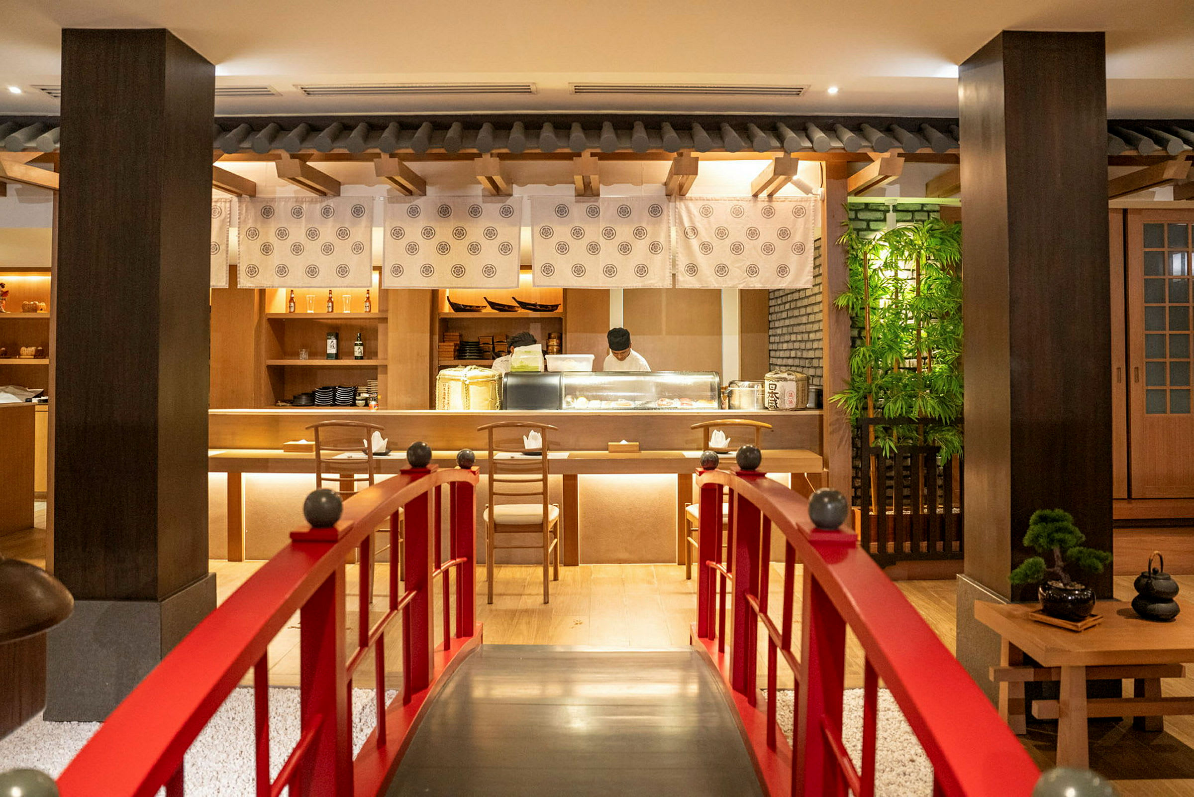 En restauranginredning med fokus på japansk stil, en röd bro leder fram till en bar där en kock arbetar. (AI-genererad text)