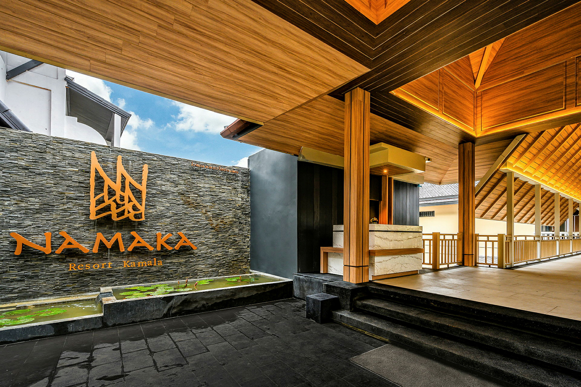 Entré till Namaka Resort Kamala med trädetaljer och stenmur. (AI-genererad text)