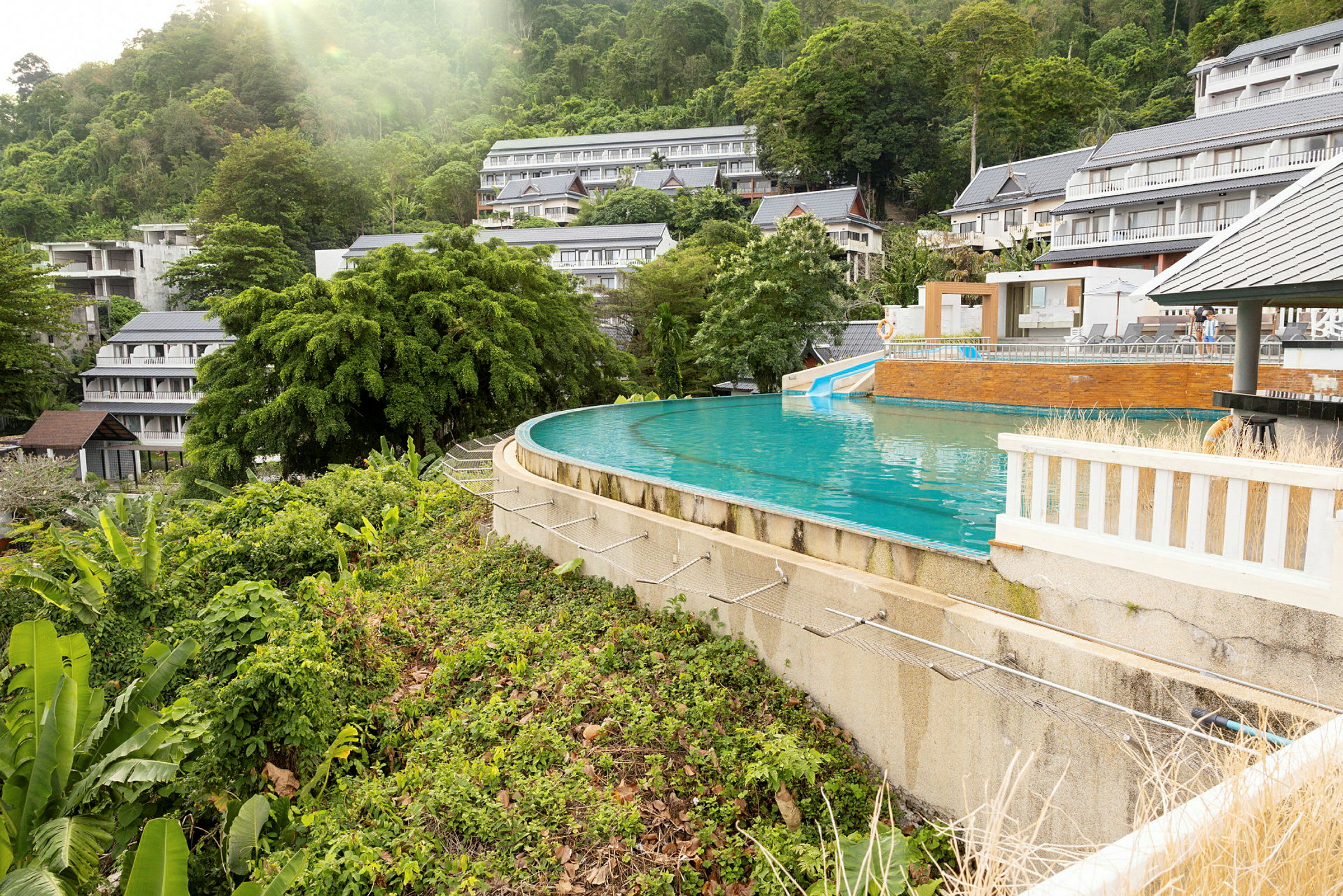 En infinitypool omgiven av grönska med hotellbyggnader i bakgrunden. (AI-genererad text)