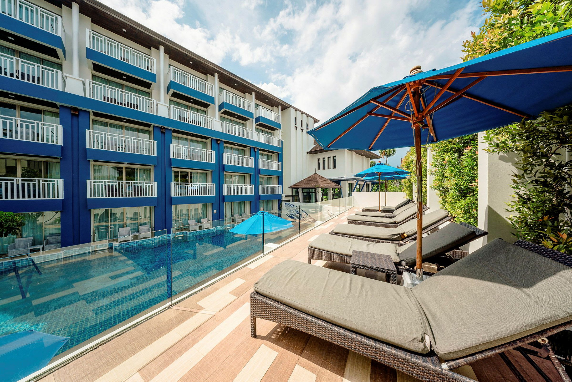 Hotellbyggnad med en pool framför, omgiven av solstolar och parasoller. (AI-genererad text)
