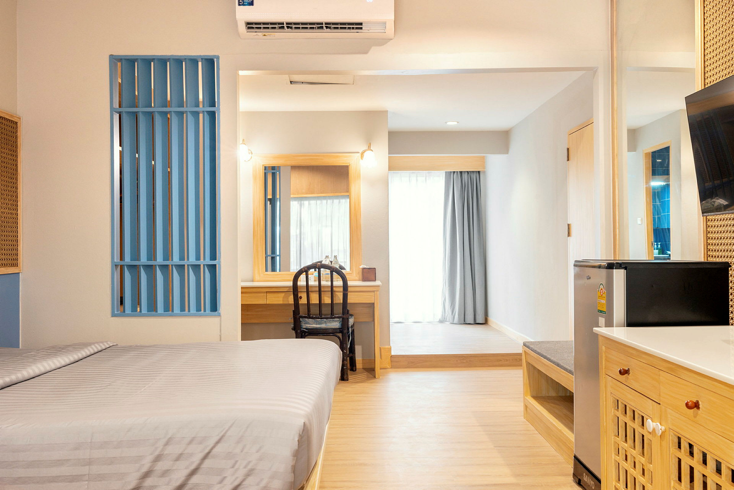 Ett hotellrum med en säng, skrivbord, stol, kylskåp och balkongdörr. (AI-genererad text)