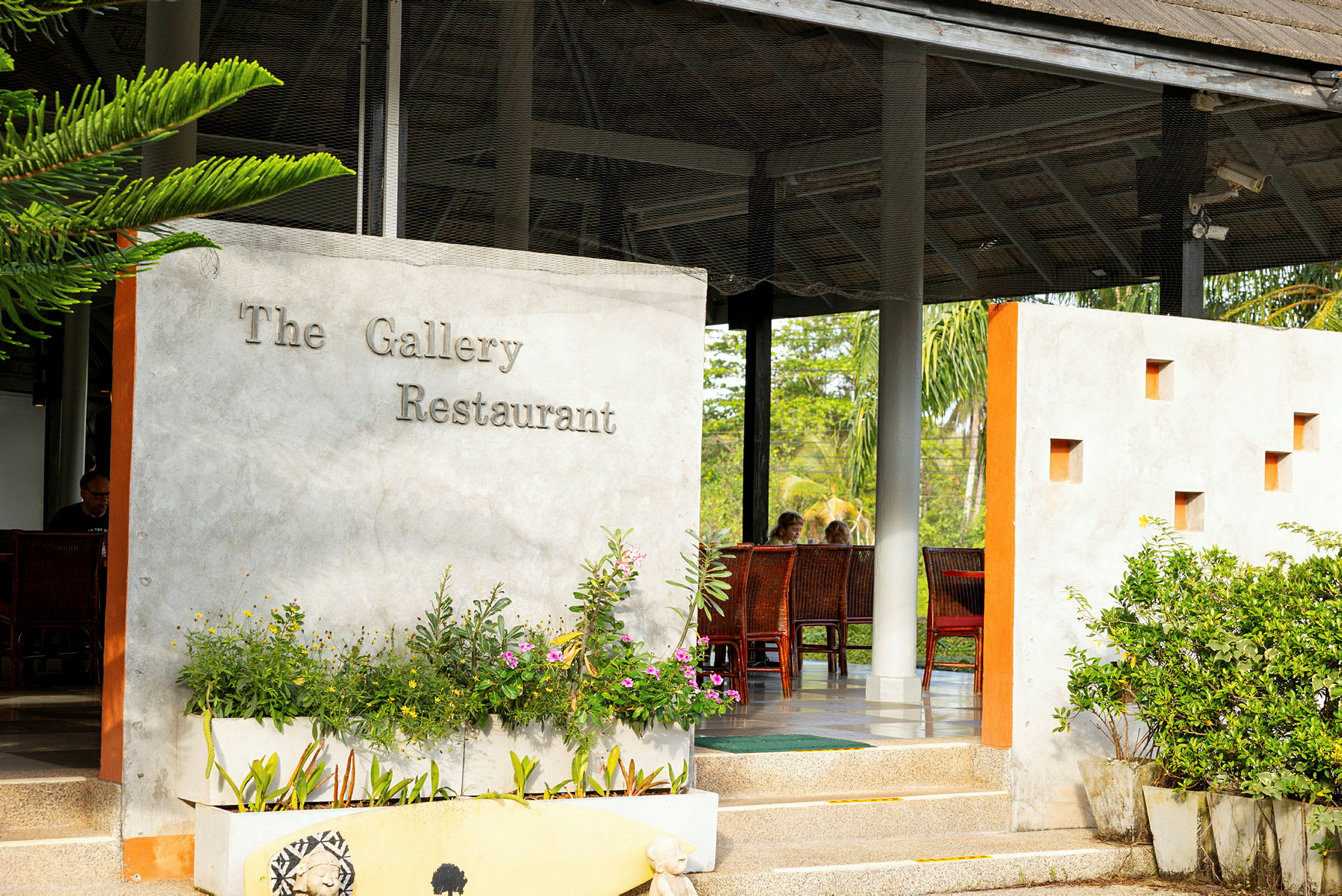Ingången till The Gallery Restaurant med växter och utomhusmöbler. (AI-genererad text)