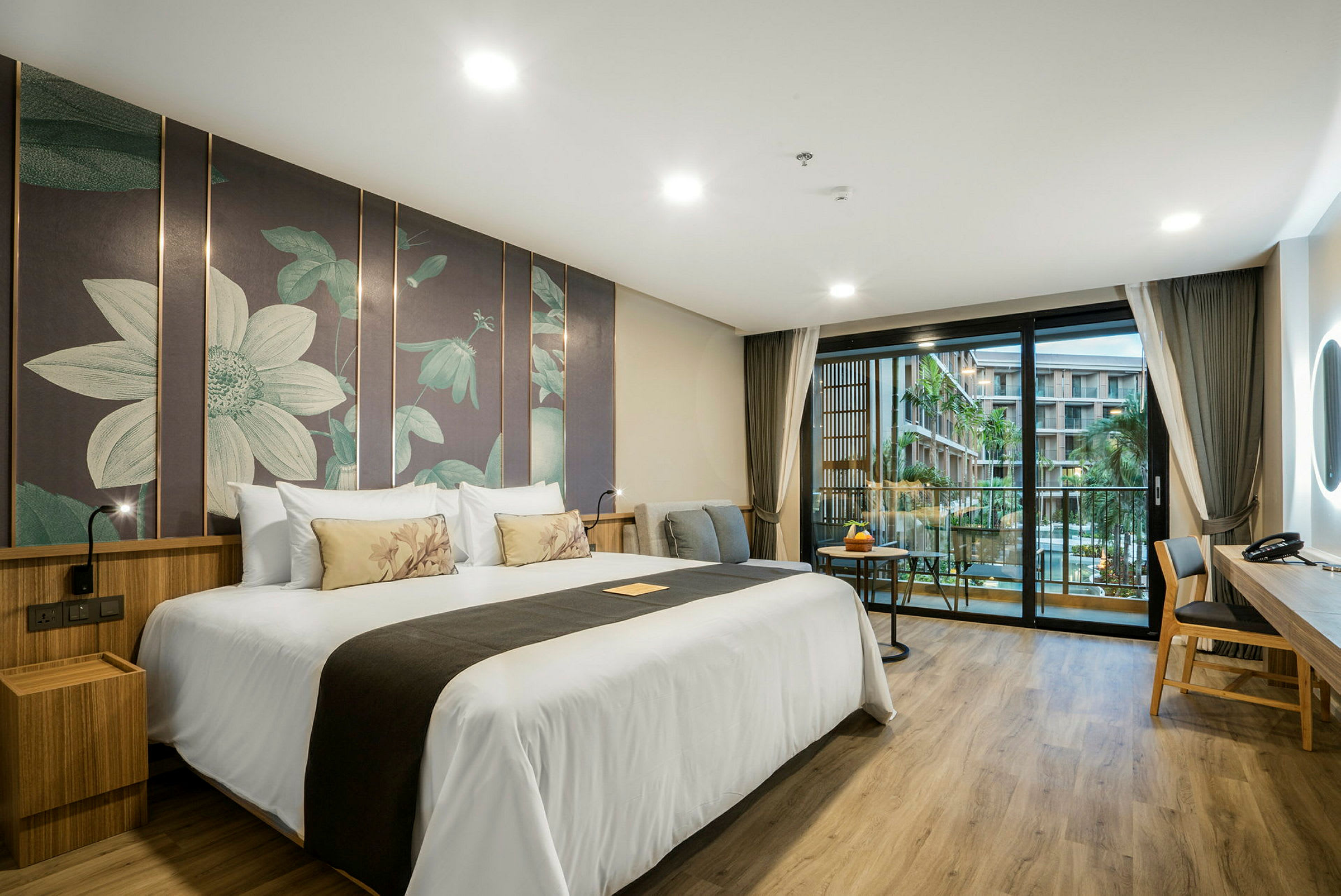 Hotellrum med en stor dubbelsäng, modern inredning och en balkong med utsikt över en pool och byggnader. (AI-genererad text)