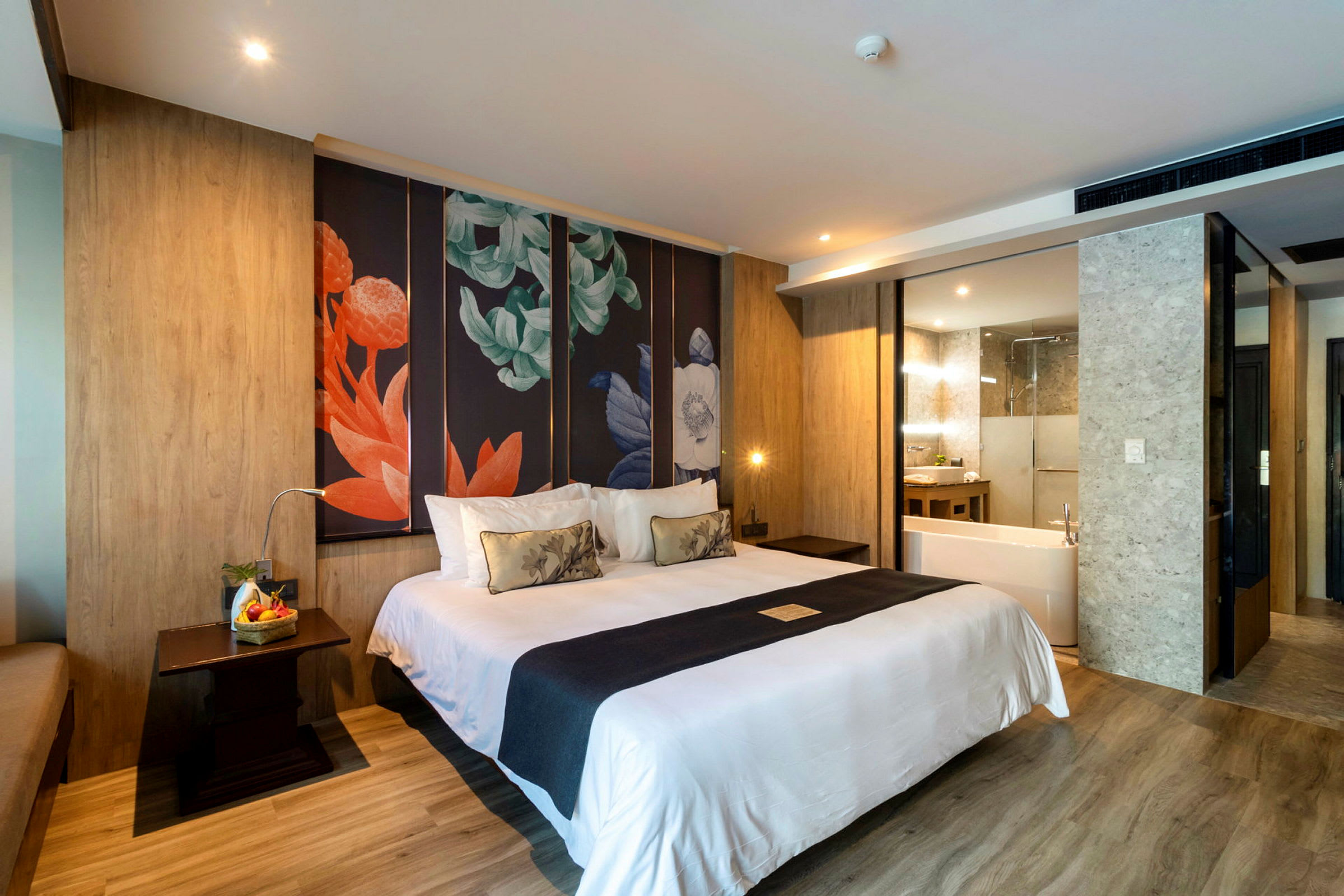 Ett hotellrum med en stor säng, dekorativ konst på väggen bakom, och ett badrum med badkar synligt i bakgrunden. (AI-genererad text)