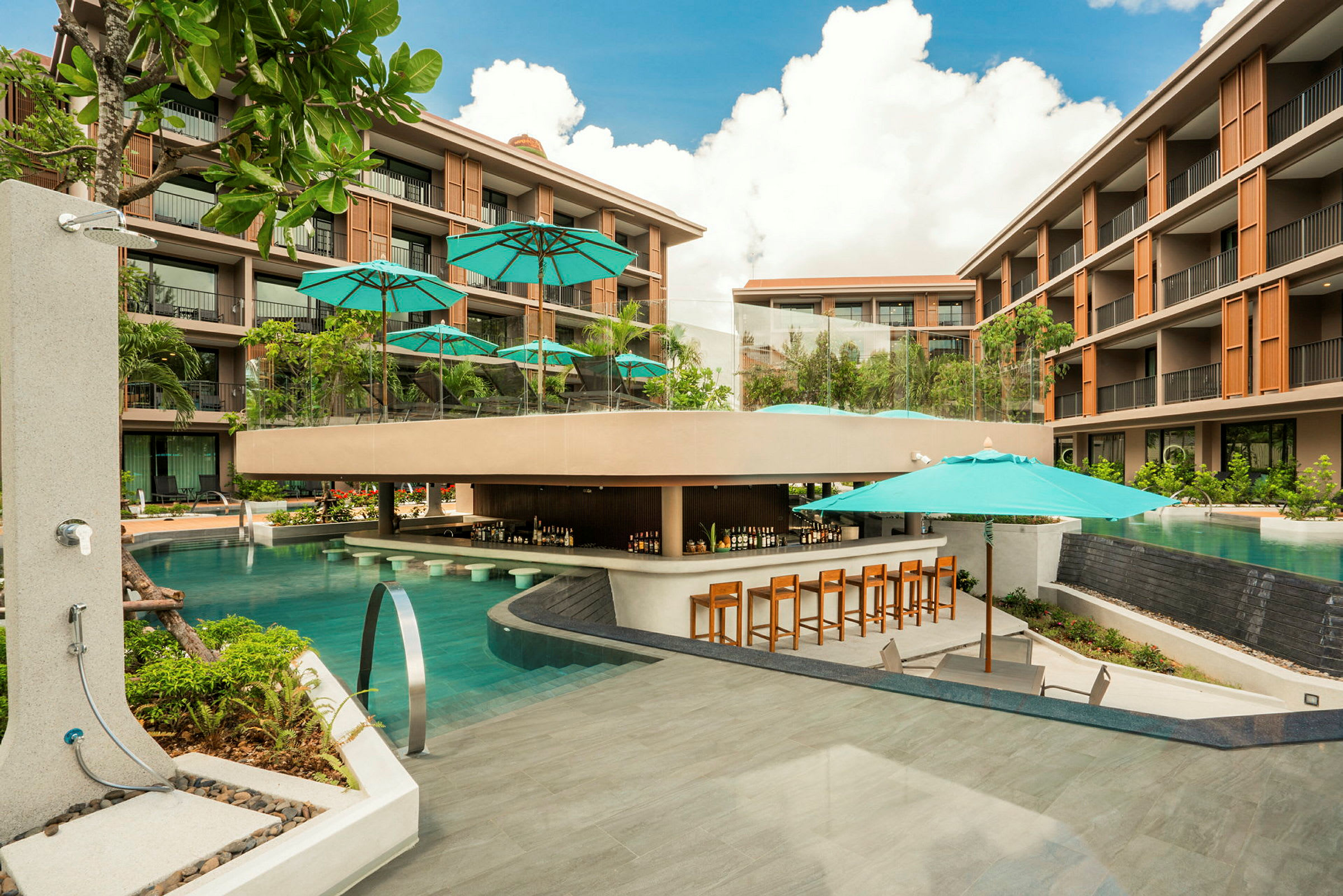 Ett modernt hotellkomplex med en stor pool som omger en poolbar, med parasoller och stolar placerade runt området. (AI-genererad text)