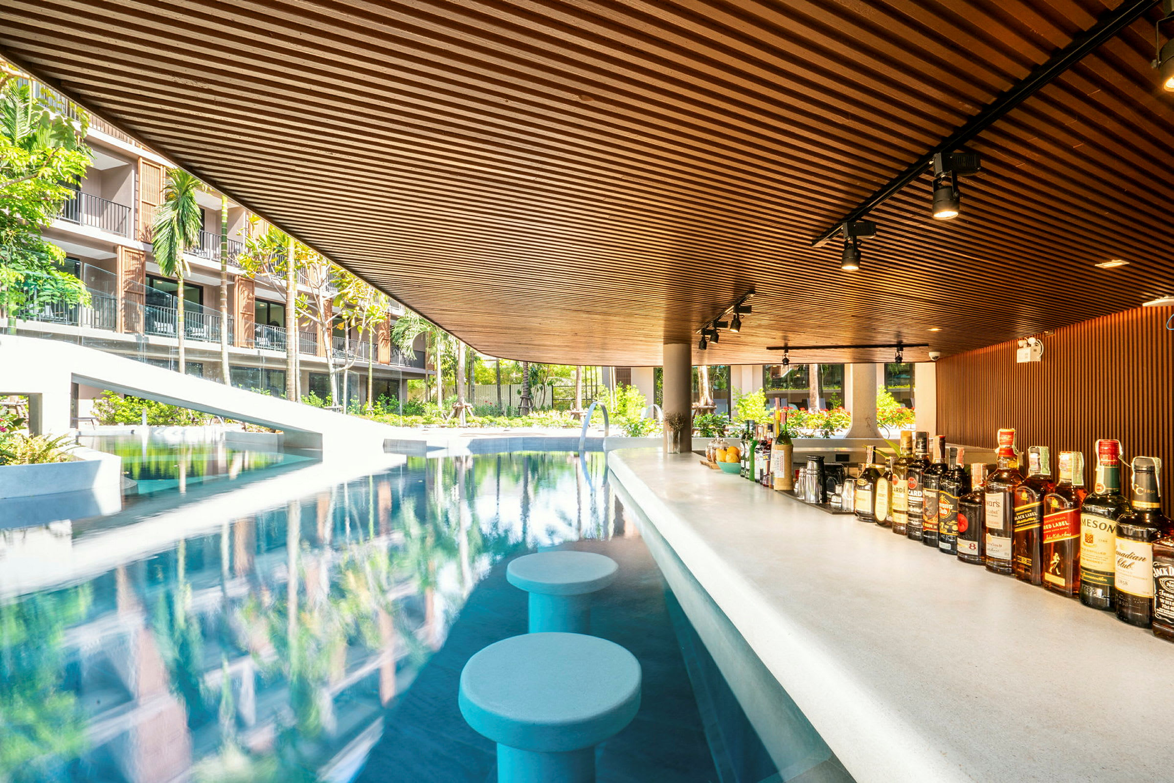En poolbar med sittplatser i vattnet, omgiven av grönska och hotellbyggnader. (AI-genererad text)