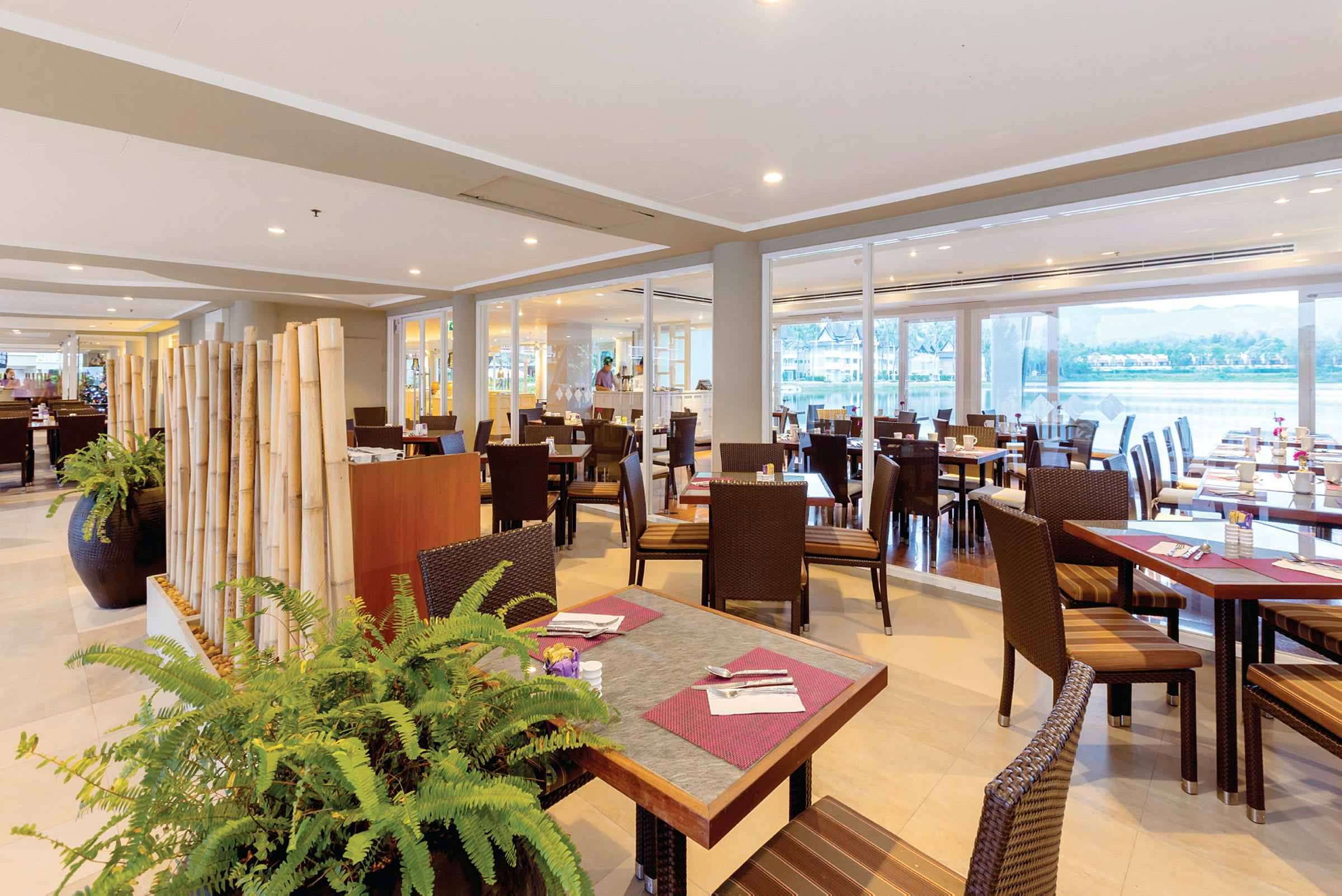 En restaurang med bord och stolar, dekorerad med bambupinnar och gröna växter. (AI-genererad text)