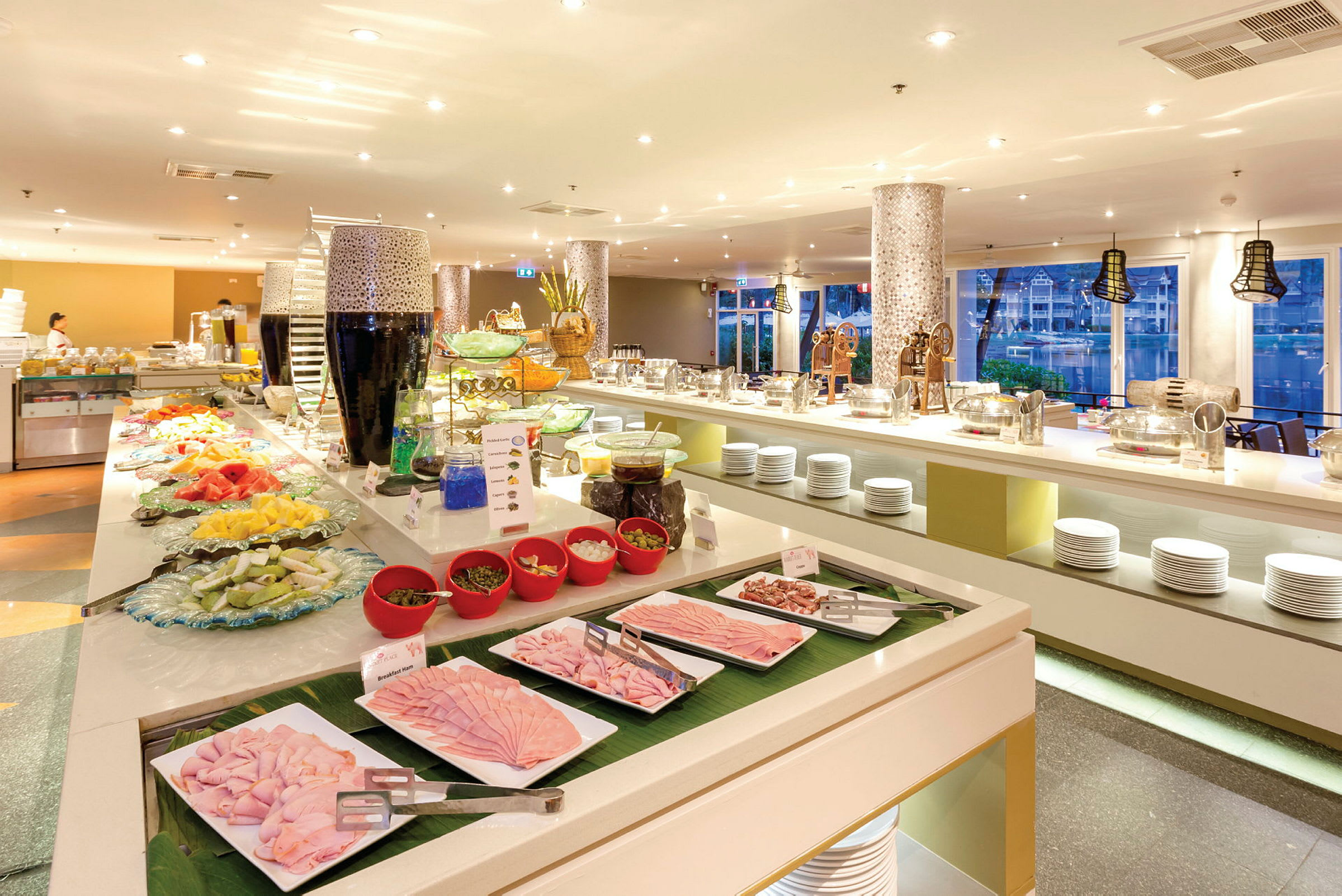 Ett hotellbuffetområde med olika maträttsalternativ upplagda samt porslin och serveringsutrustning. (AI-genererad text)